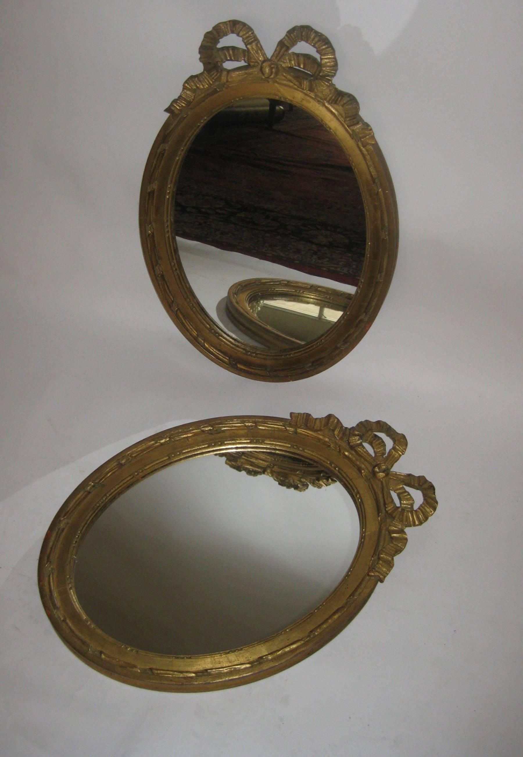Pair of gilded French oval shaped mirrors highlighted with a pierced carved cartouche depicting tied ribbon upon a graceful frame adorned with twisted ribbon pattern. The giltwood frames retain the original finish with lovely patina. It is unusual