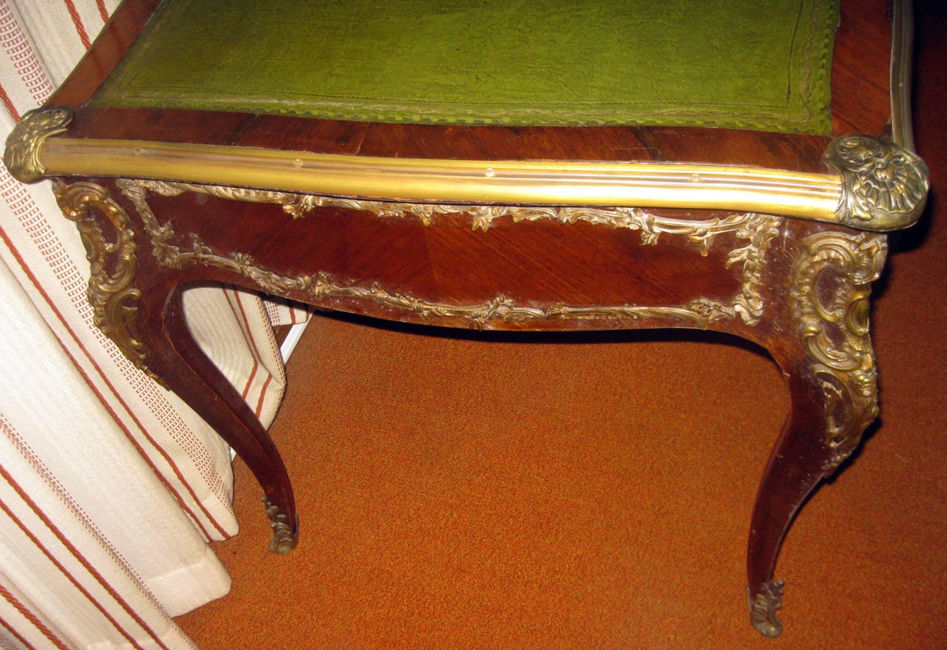 Handsome large size French writing table made of kingwood and featuring a Moroccan leather top, foliate bronze ormolu mounts, cabriole legs and three drawers. The desk is finished on all sides. Nice old patina on ormolu.