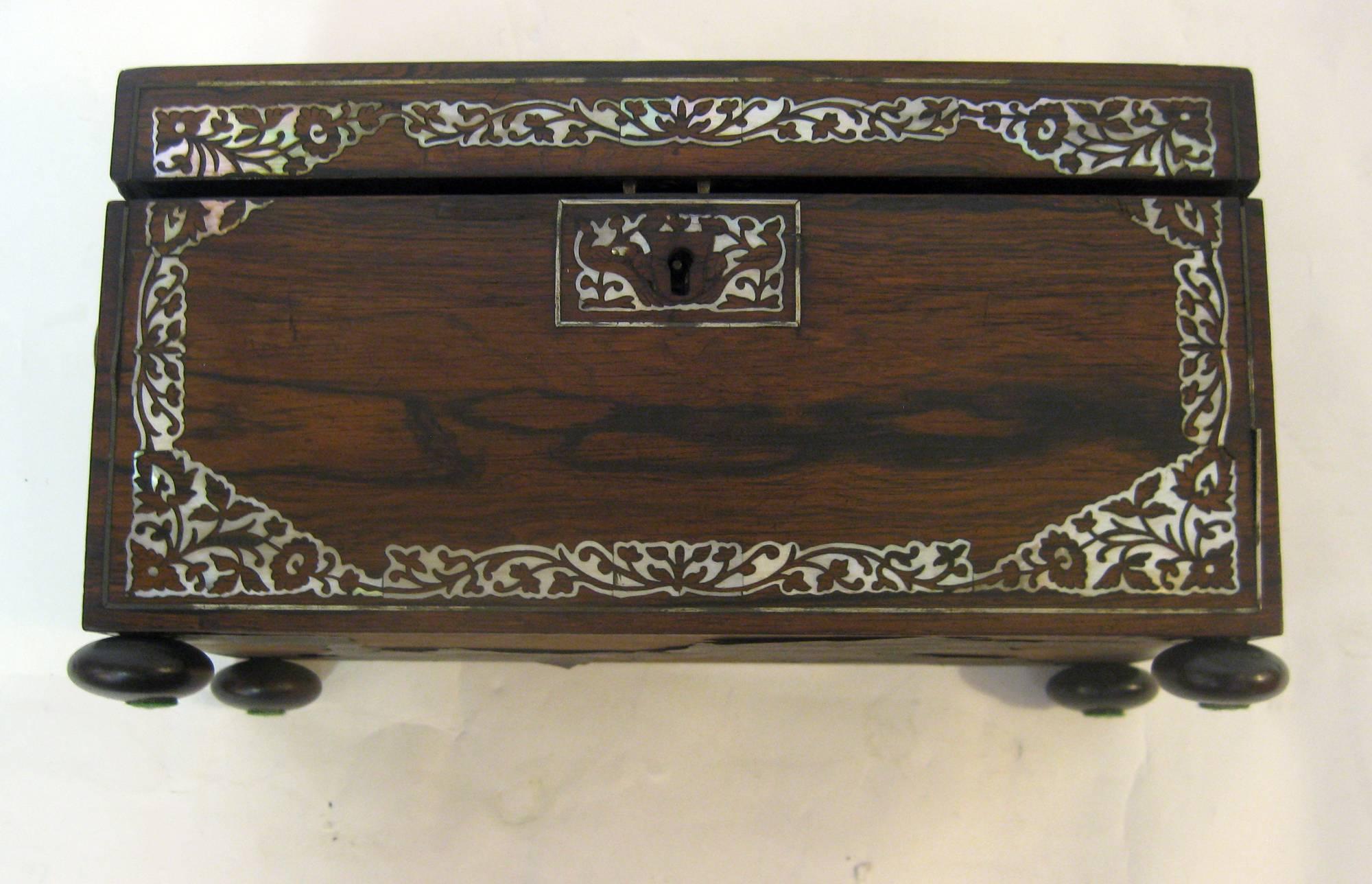 Tea Caddy made of rosewood with extensive mother-of-pearl decoration to the top and front. Special features include bun feet and unusual handles on either side with mother-of-pearl buttons. The interior has two hinged lidded canisters and a center