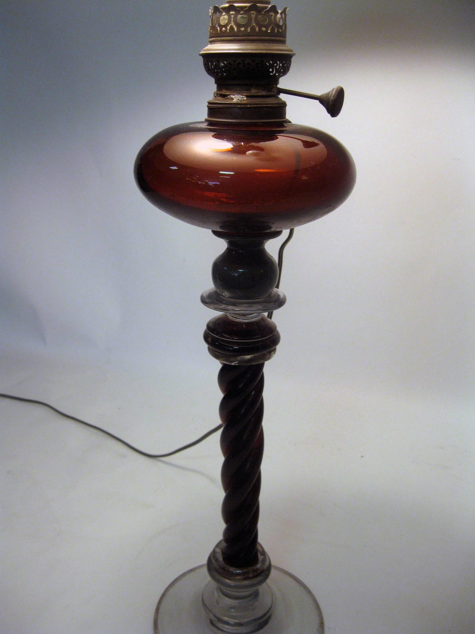 This unusually tall antique American glass oil lamp features a tall ruby colored twisted rope column extending to a ruby font. The round base and middle pieces are clear glass. Brass fittings. It has been converted to electric and is in good working