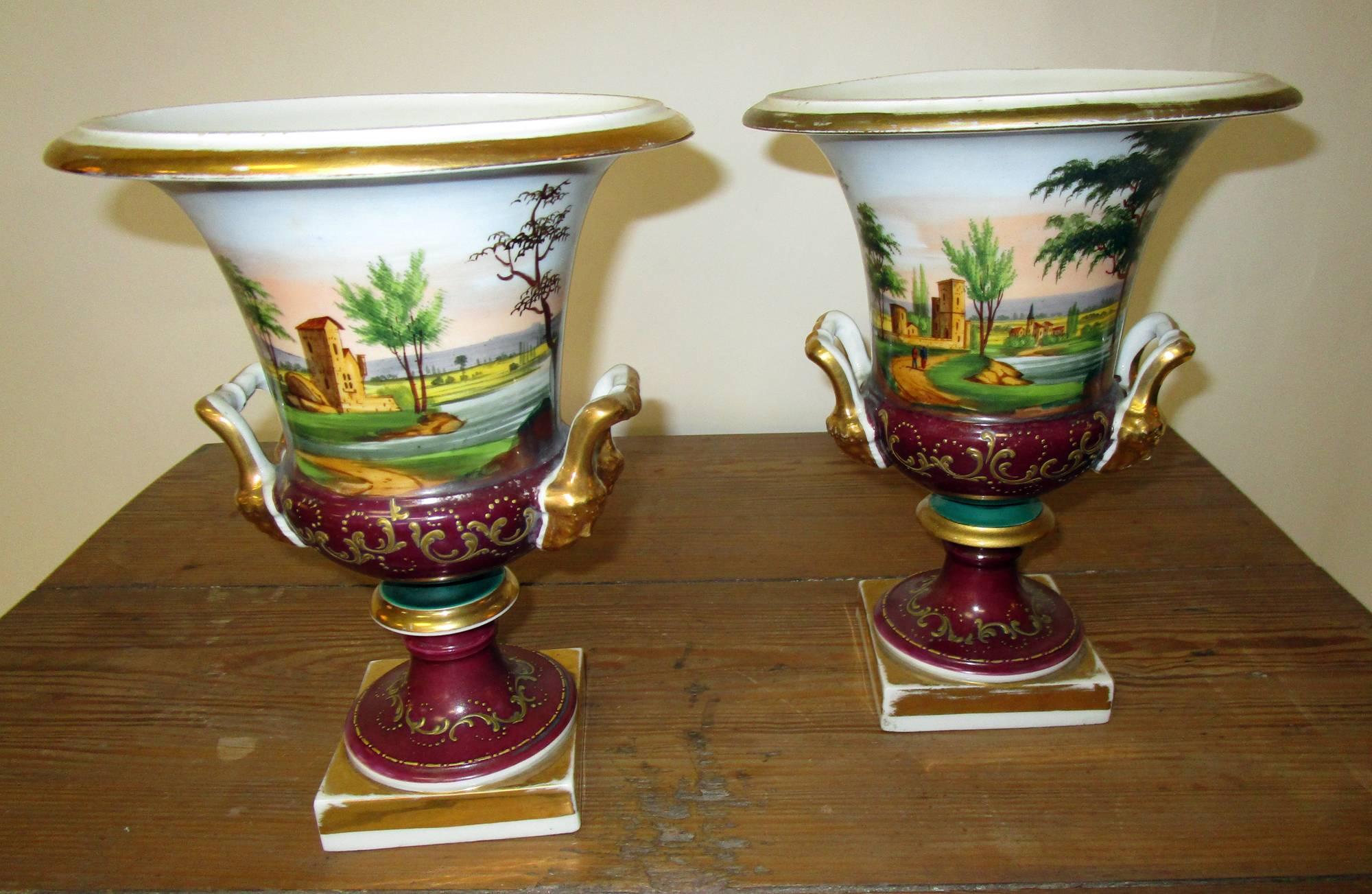 Hard paste porcelain with polychrome and gold leaf - iron bolt. Impasto decoration. Lovely colors. These classical form urns are clearly a pair, but not an identical pair. Each has a rustic scene with a different structure on each side. Bisque heads