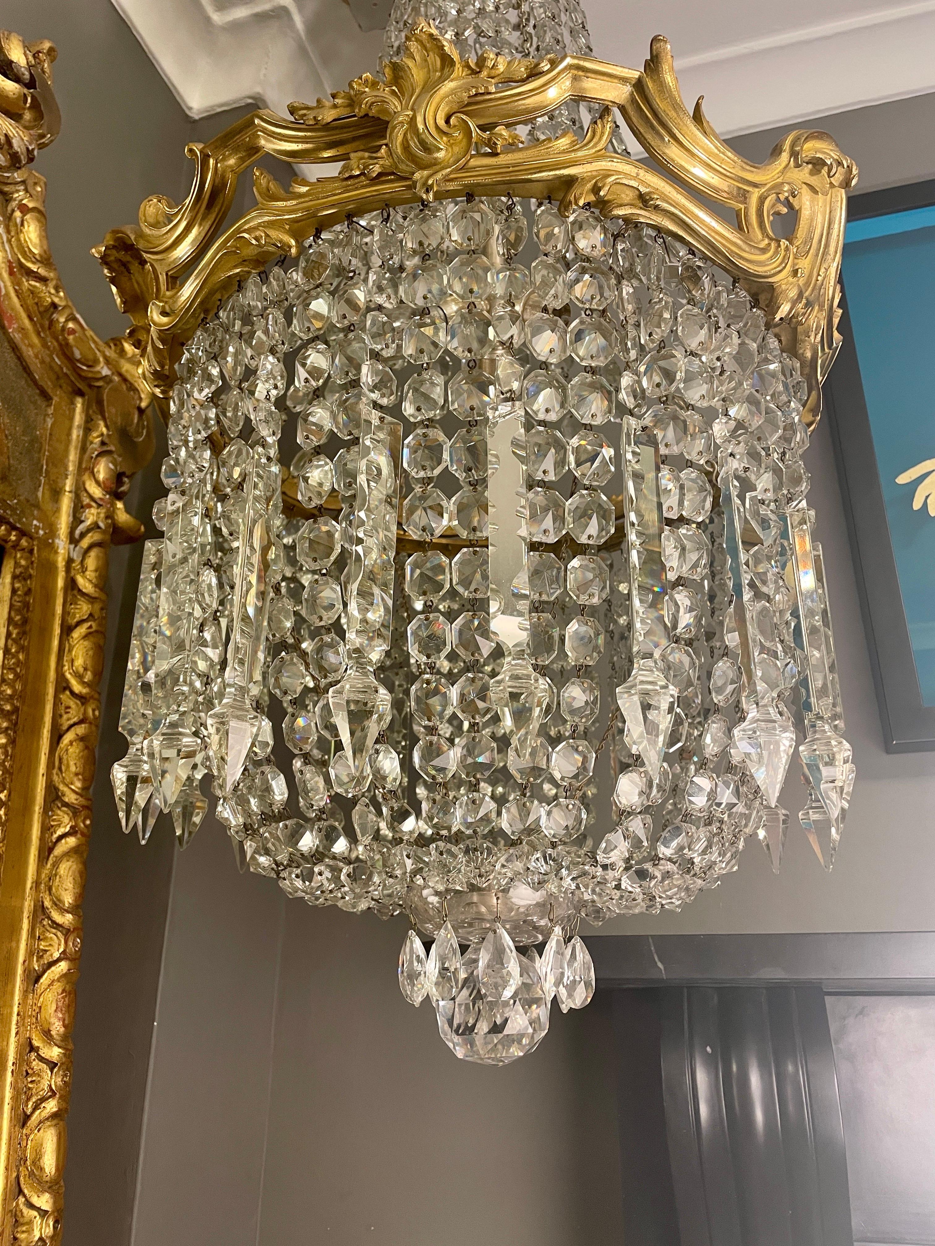 A large tent and purse style French gilt bronze and crystal chandelier. Made in the Rococo Louis XV taste, with the gilt bronze frame with sweeping scrolls of foliate acanthus and feather cartouches. The top tent of beaded crystal the lower purse