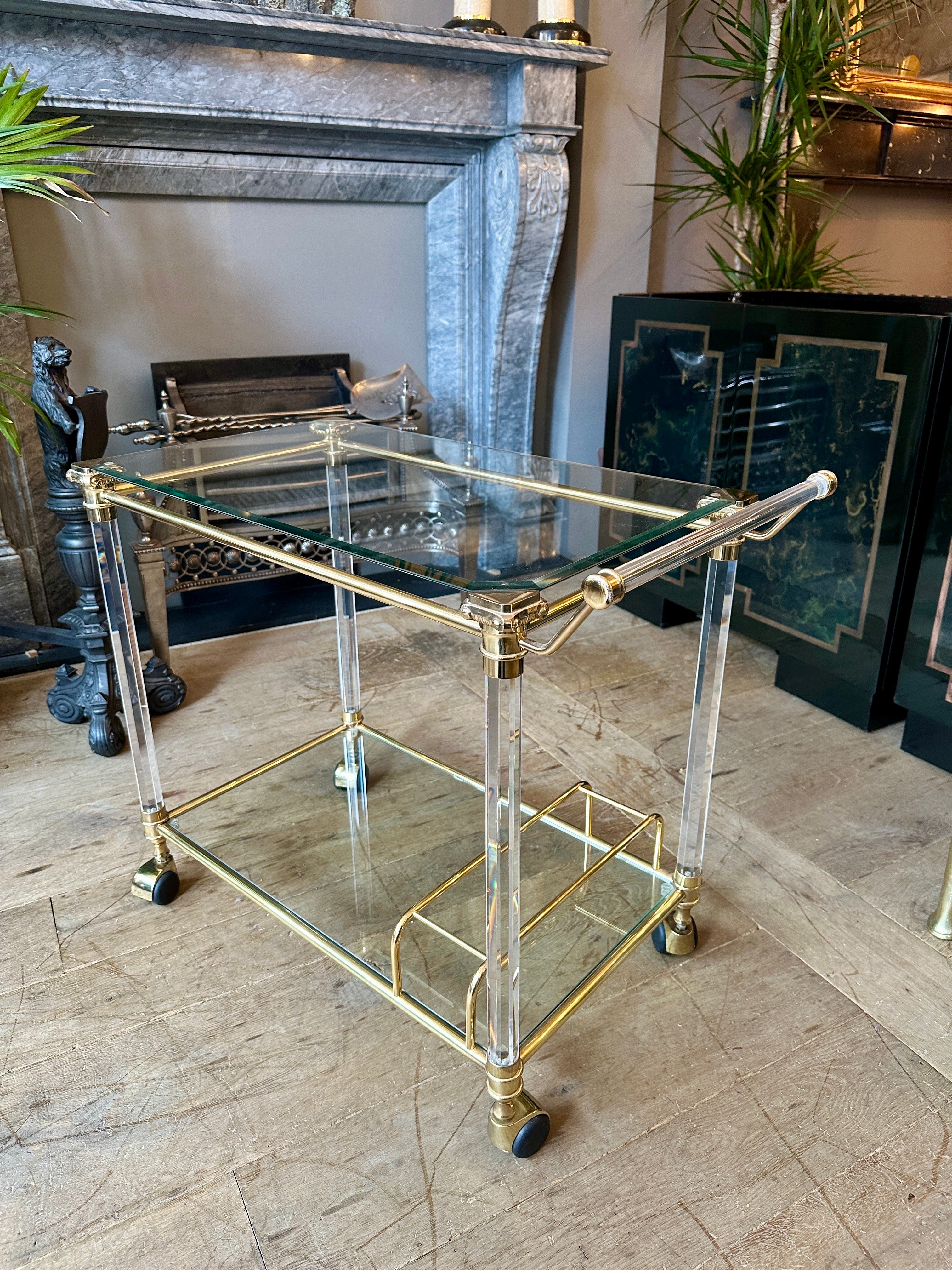 A late 20th century bar car or drinks trolly in lacquered brass and lucite. The Octagonal columned supports with decorative Corinthian capital supports. Elegant yet simple handle and stretchers. Two tiered with bottle section on bottom tier.