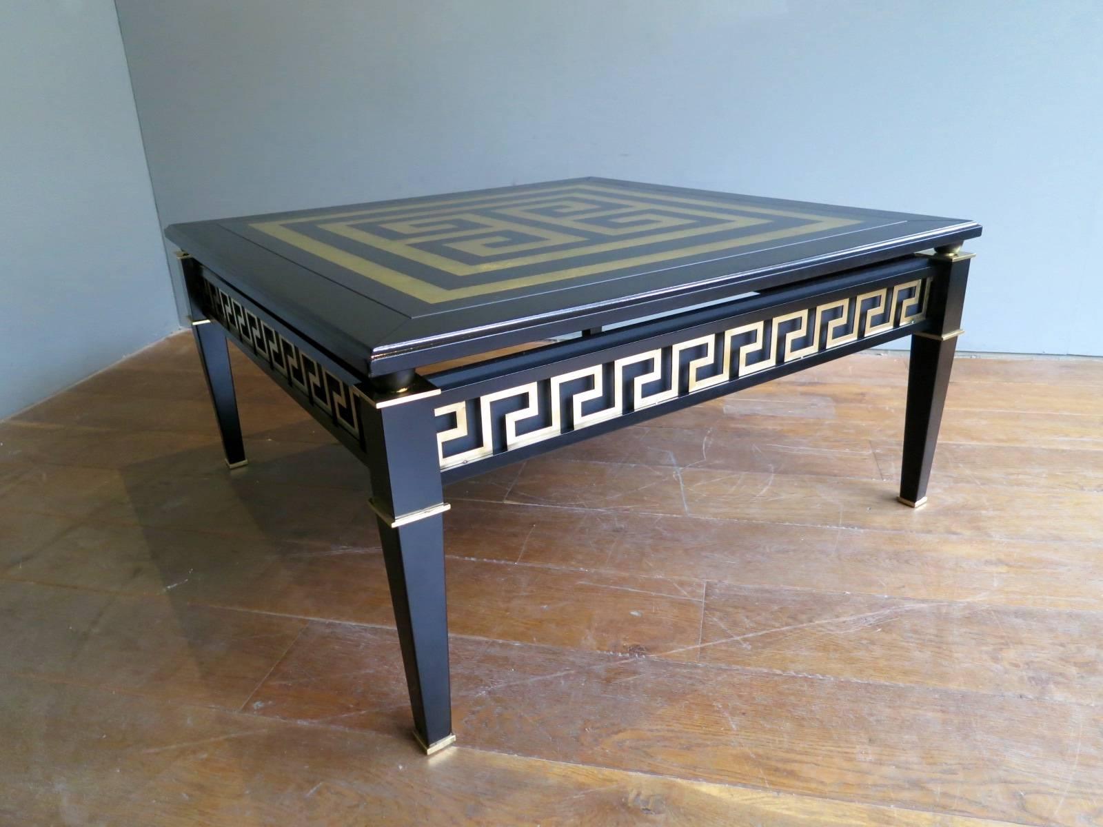 A large sophisticated square coffee table, with Verre églomisé Greek key top, raised on brass spacers from an ebonized frame with brass Greek key fretwork and brass accents. In fantastic condition. Very much in the manner of Maison Jansen.