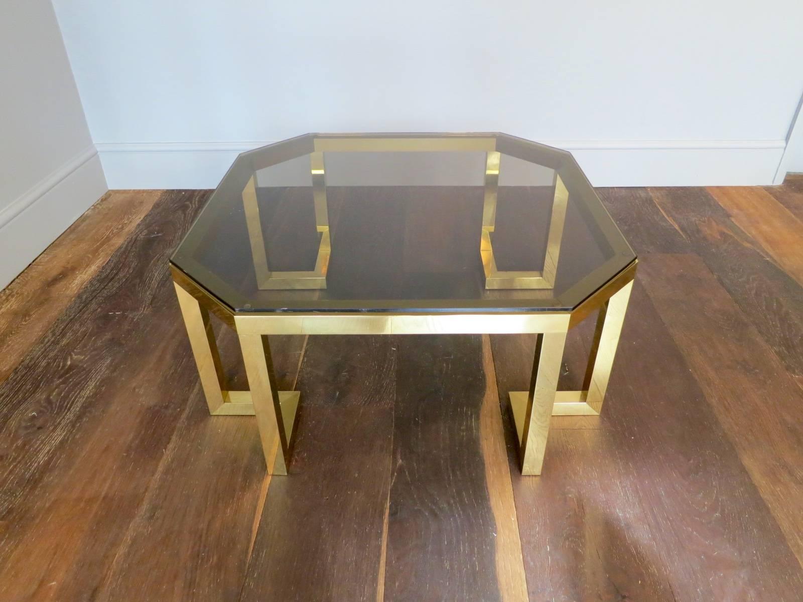 An octagonal table in brass with shaped smoked glass top and inverted supports, in very condition and exceptional quality.