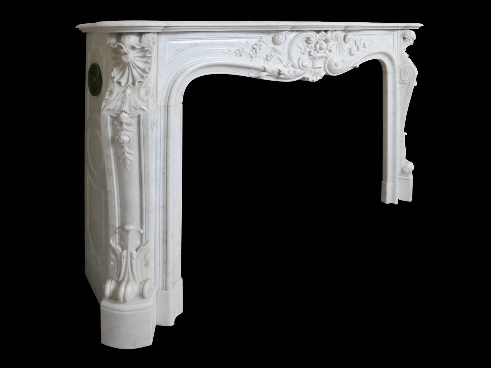 A well proportioned and finely carved Louis XV style fireplace in Italian Carrara marble. The carved panelled jambs with stiff acanthus at the bottom, descending flowers and foliage surmounted by C-scrolls and shells. The panelled side returns