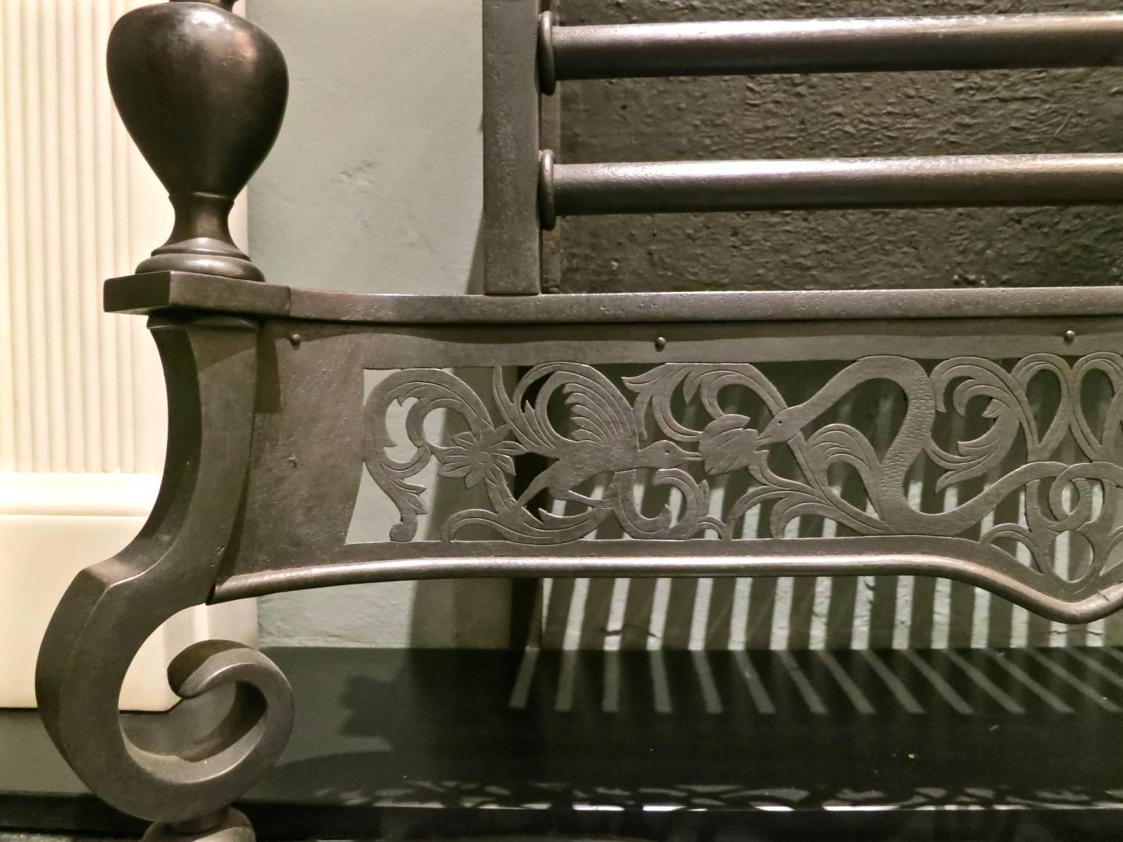 A well proportioned decorative fire grate in the Georgian manner, with large finials supported on scrolled feet flanking intricately pierced fret work of intertwined serpents and birds. The two bar burning area with conforming finial detail,