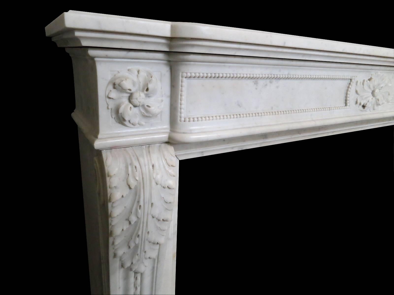 A large Louis XVI style 19th century surround in Italian Carrara marble. The carved acanthus leaf console jambs having tapering rope twist panels, terminating in scrolls. The bowed frieze with carved elliptical paterae to centre, flanked on either