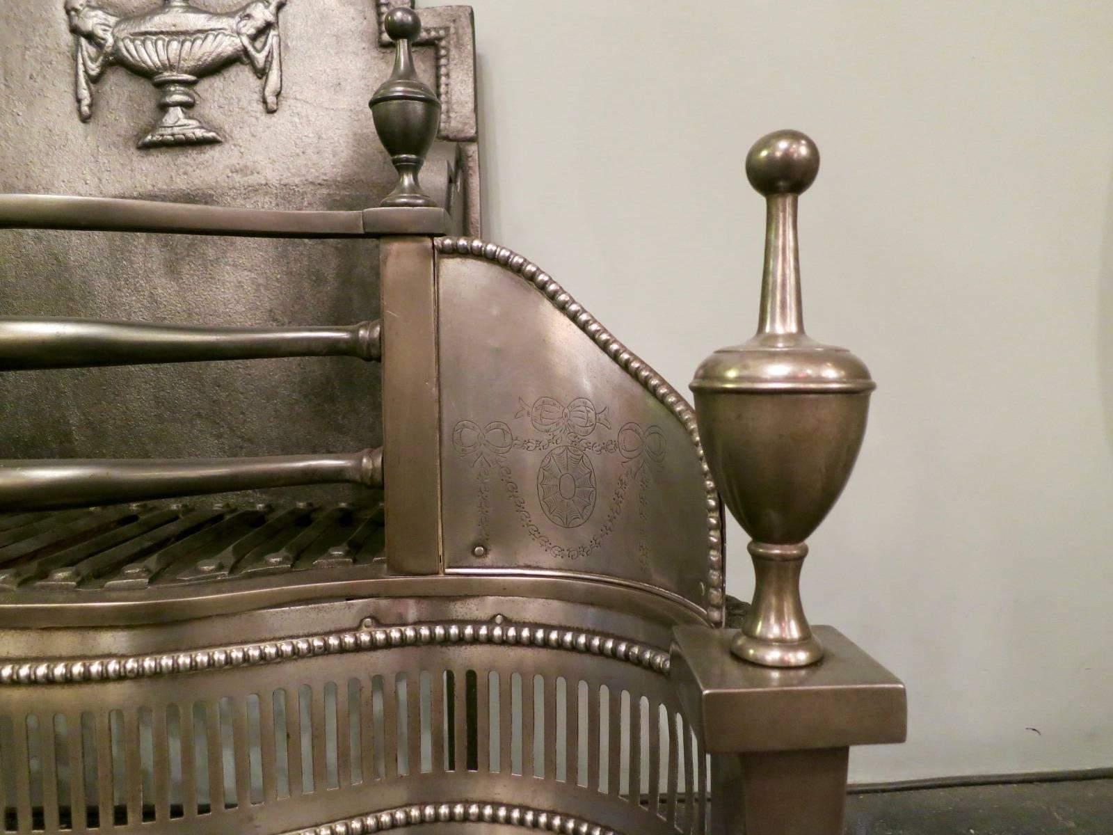 A large fire grate in the Georgian style, with tapering column legs surmounted by spherical lidded urns. The beaded spandrels with classical engravings, below the serpentine pierced fluted fret work again edged in beading. A decorative cast iron
