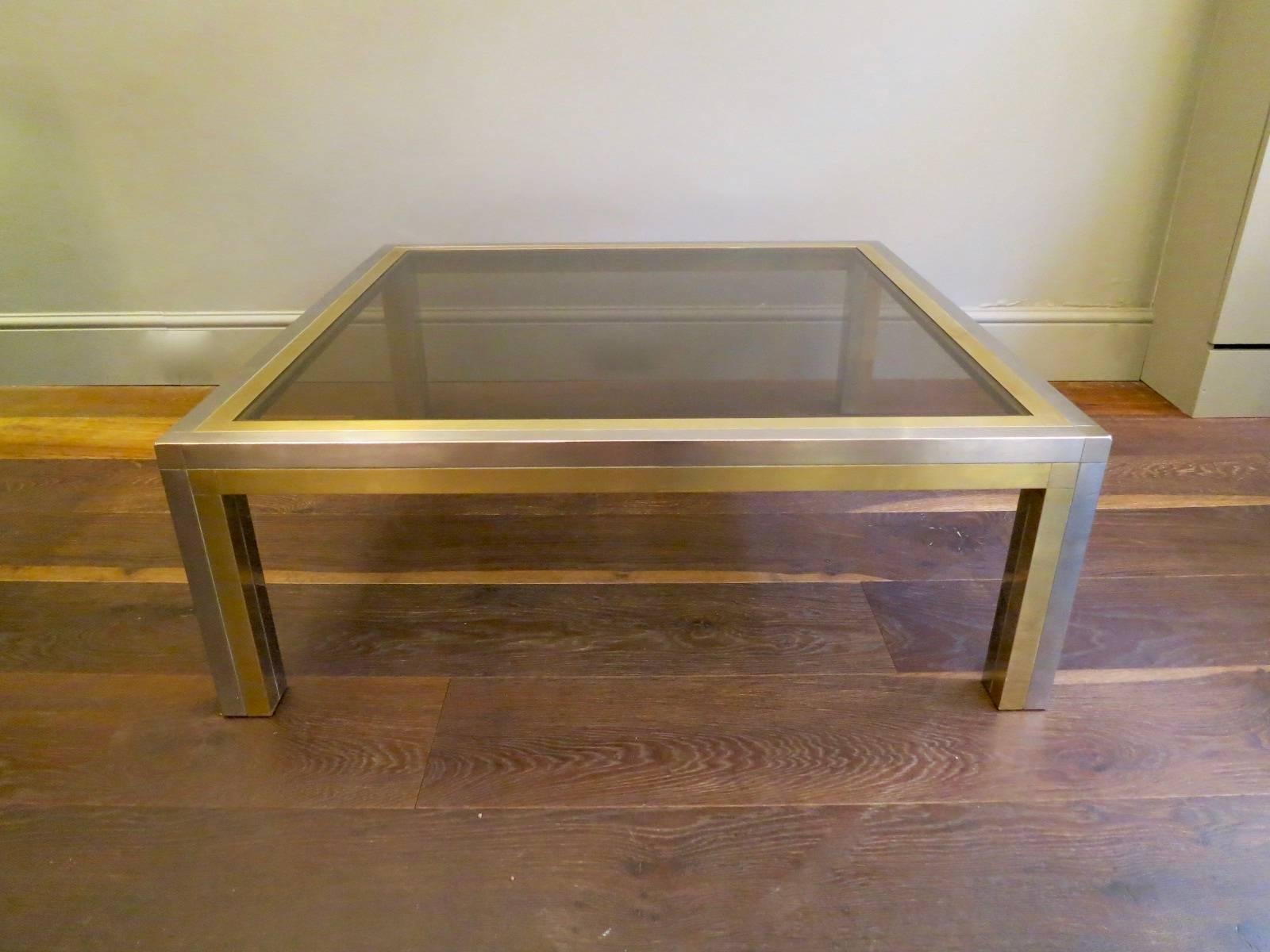A large and low square coffee table, in brass and chrome with original smoked glass top. In the manner of Romeo Rega.
