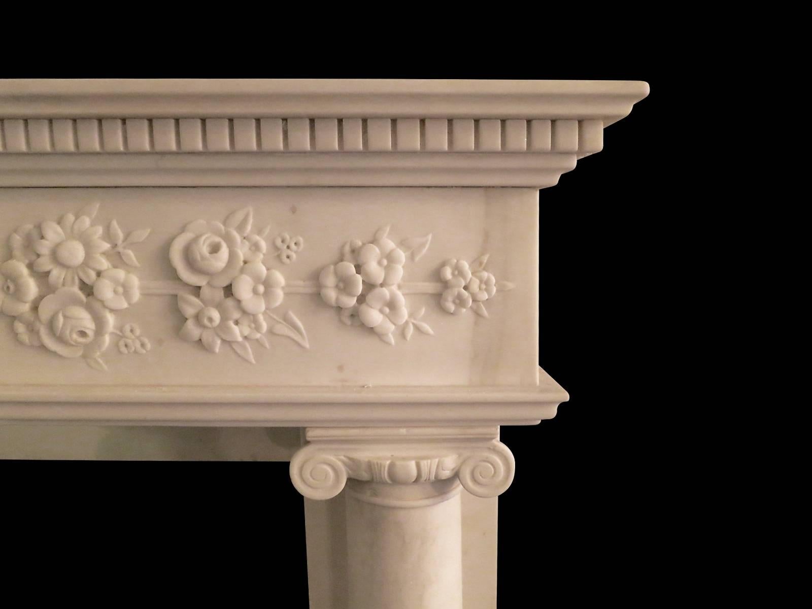 A 19th century English Regency fireplace of compact proportions in Italian Statuary white marble. The columned supports, on simple foot blocks and Socles, surmounted with Ionic Capitals. The Frieze carved from end to end with foliage, flowers and
