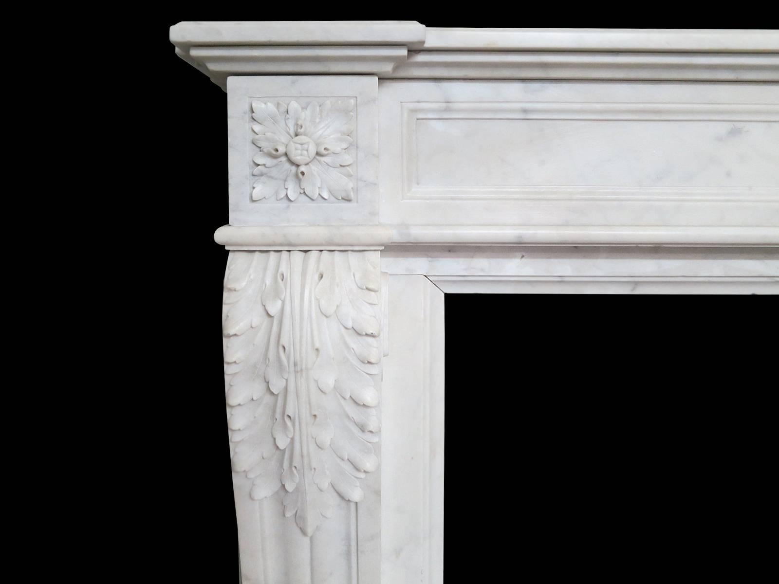 A 19th century Louis XVI style fireplace in Italian Carrara marble. The frieze with carved oval patarae to centre with fielded panels on either side. The end blocks again of carved patarae atop acanthus leaf carving on console shaped jambs. Having