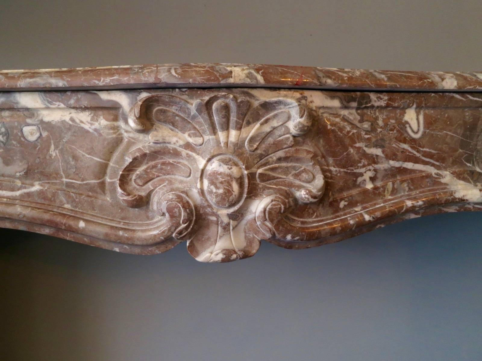 An antique surround in Rouge Royal Marble in the Louis XV manner with carved shell to centre and scrolled moulding from the foot block to end of frieze. Late 19th century. Imported from Paris.