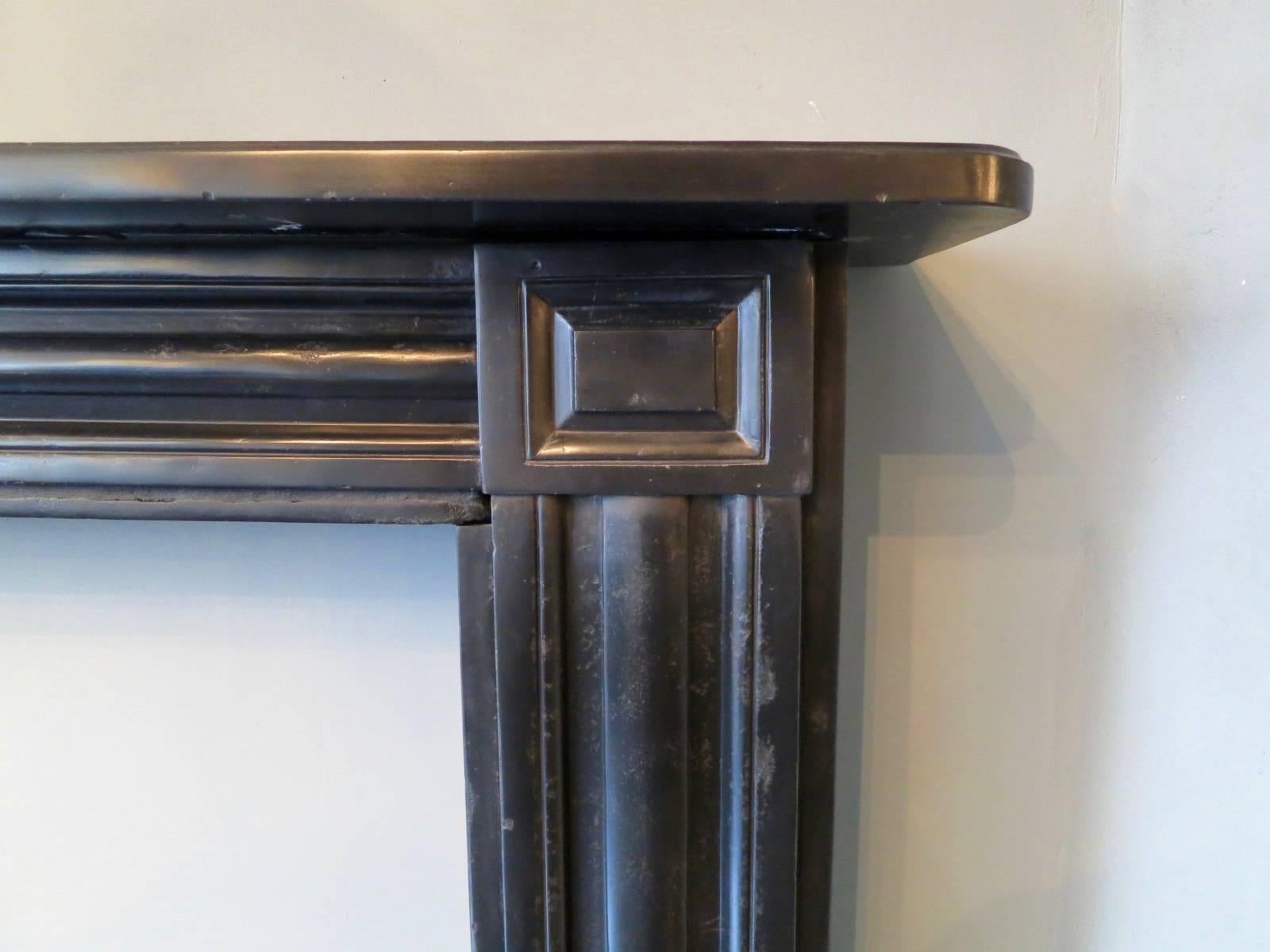A large English antique fireplace from the Regency period in Belgian black marble, with moulded panels to jambs and conforming frieze. A Simply moulded lip to shelf and square fielded corner blocks. All supported from square foot blocks. This