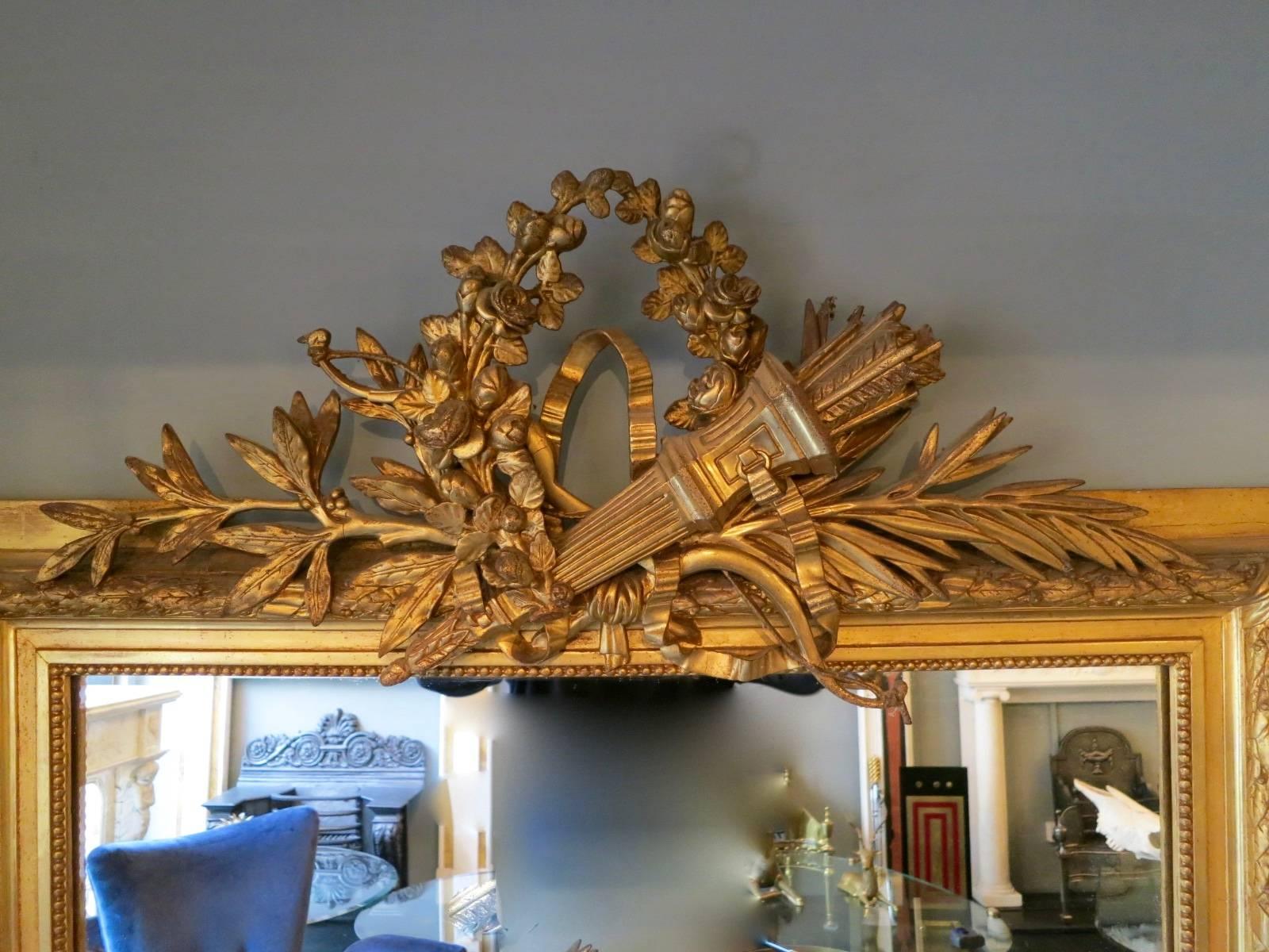 A tall overmantel mirror from the late 19th century, with a large cartouche of bow and quill. Retaining its original mirror plate.
