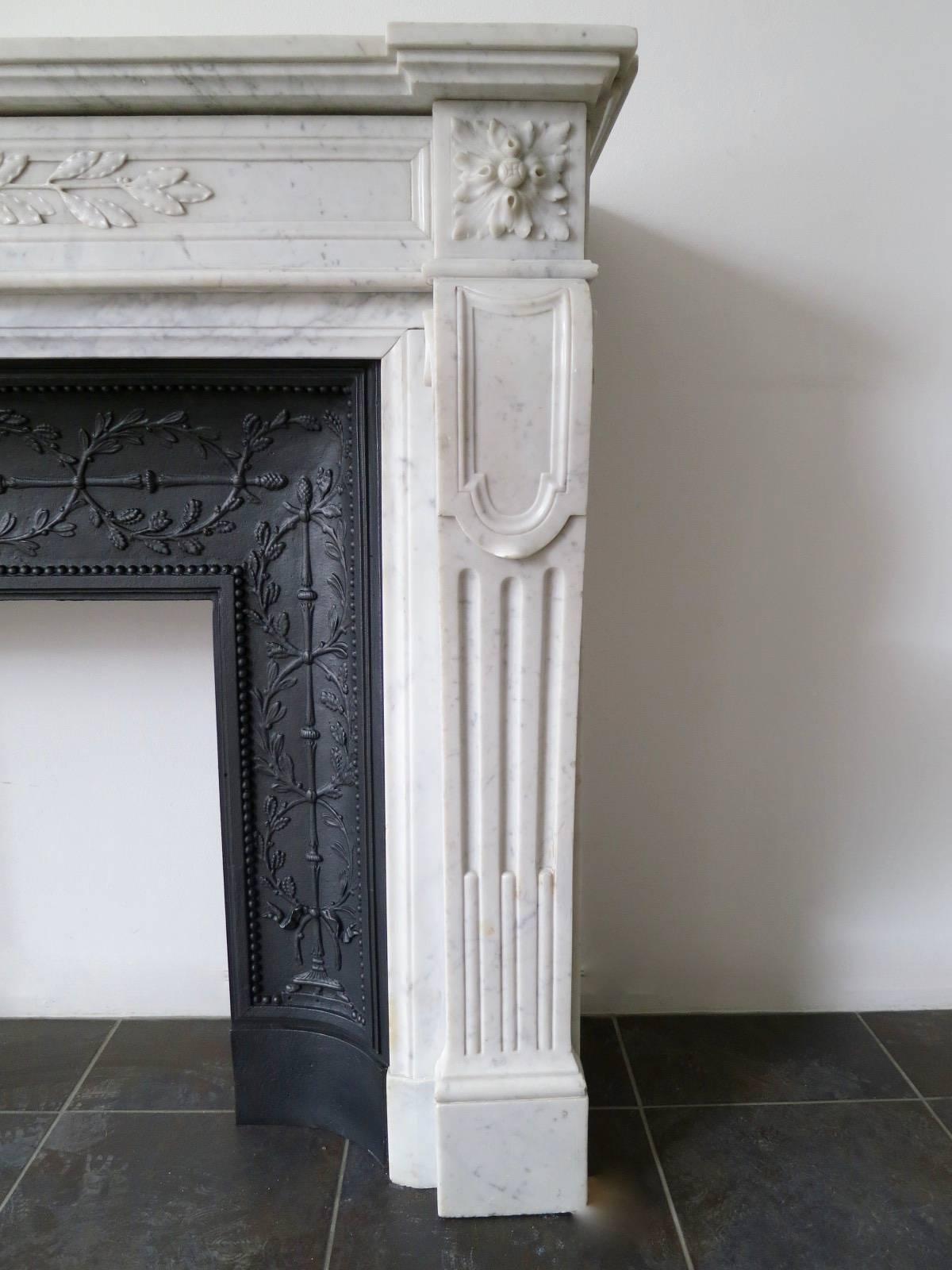 A well carved and proportioned Louis XVI style mantel in pale Carrara Marble from the mid-19th century. The fluted console jambs surmounted by square carved patarae, flanking a carved frieze of laurel leaf and garland. A breakfront mantle with under