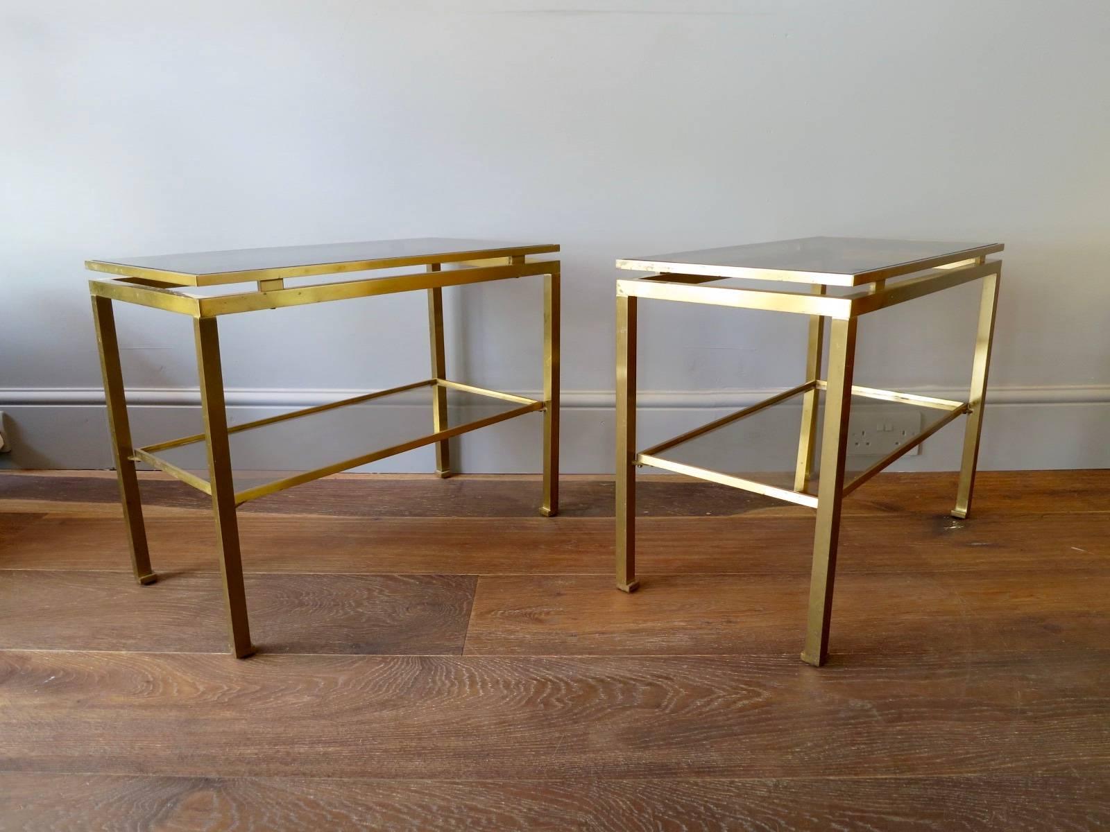 A pair of lacquered brass two tiered side tables by Guy Lefevre for Iconic design house Maison Jansen. The glass tops slightly tinted, the brass with some authentic patination, France.