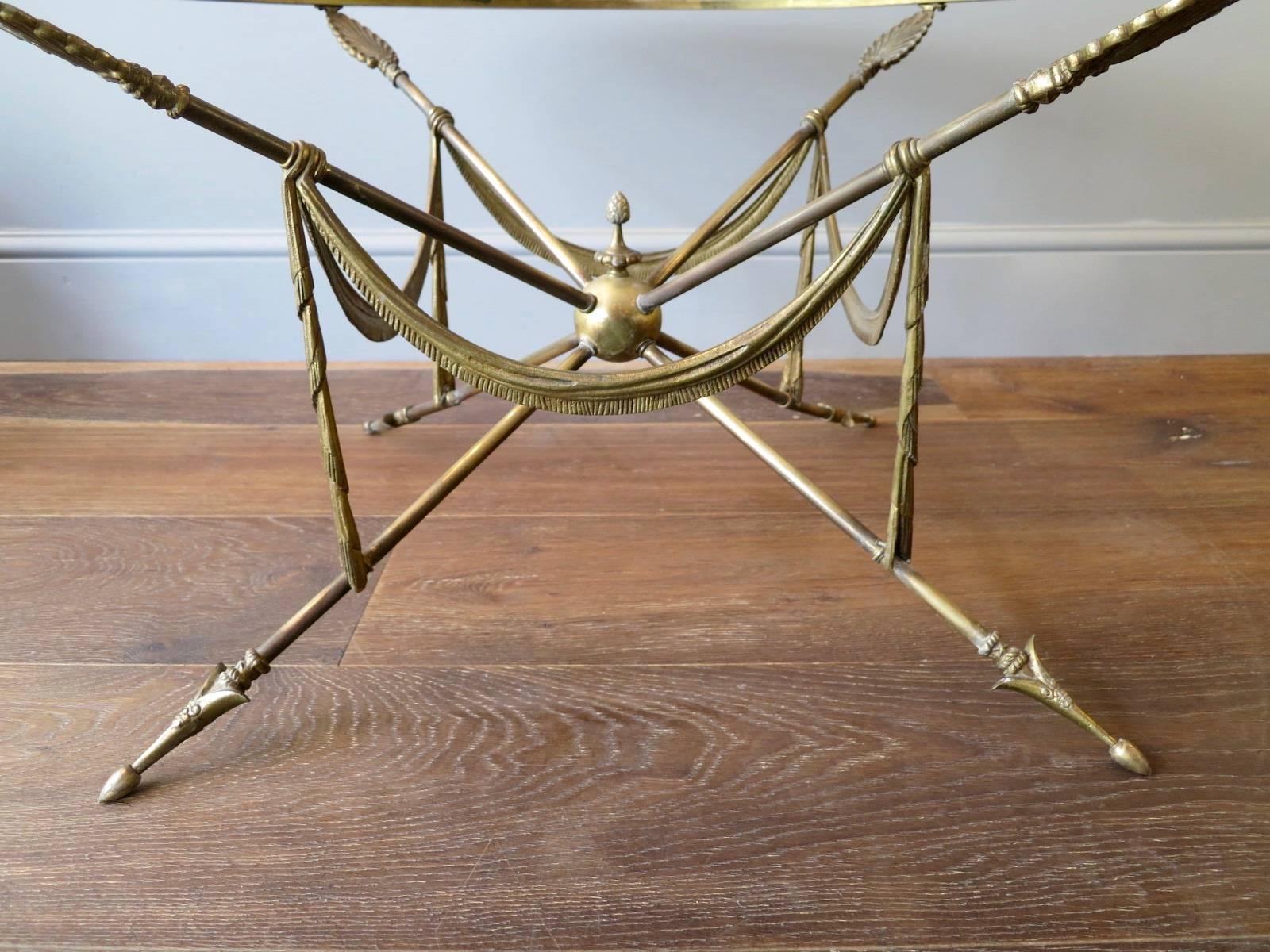 A circular cocktail table, attributed to Maison Jansen. Designed in the neoclassical style from the mid-20th century. The central sphere supporting the legs with arrow dart feet and feather supports at top. The drapery hanging from the supports.