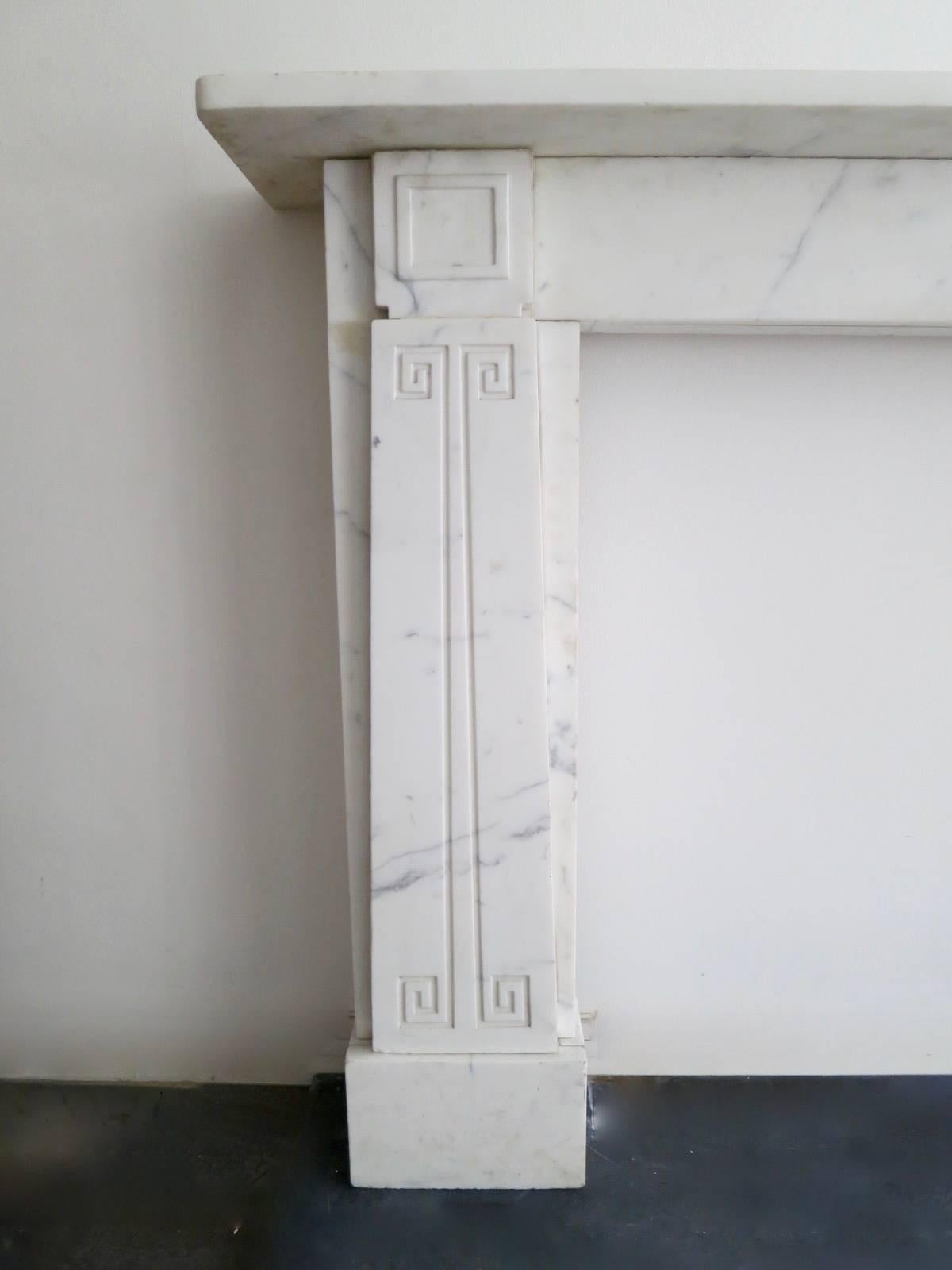 A Soane style fireplace in Italian veined white marble, with tapering Greek key decorated jamb panels. Square panelled end blocks, with simple frieze and shelf. All supported on large square foot blocks, mid-late 20th century.