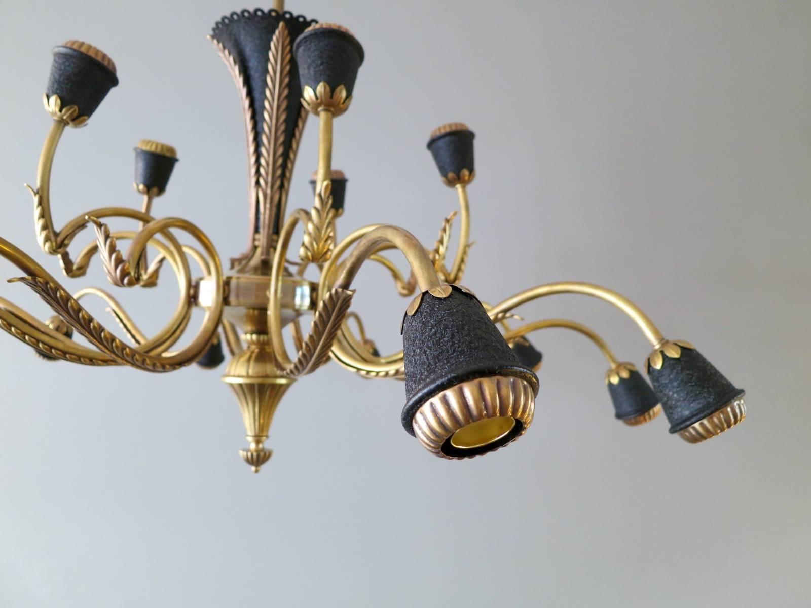 A large fourteen-arm brass and textured black accents chandelier from the mid-20th century. The foliate detail to arms and bulb holders conforming with the body of the light. A very good quality and well restored piece.