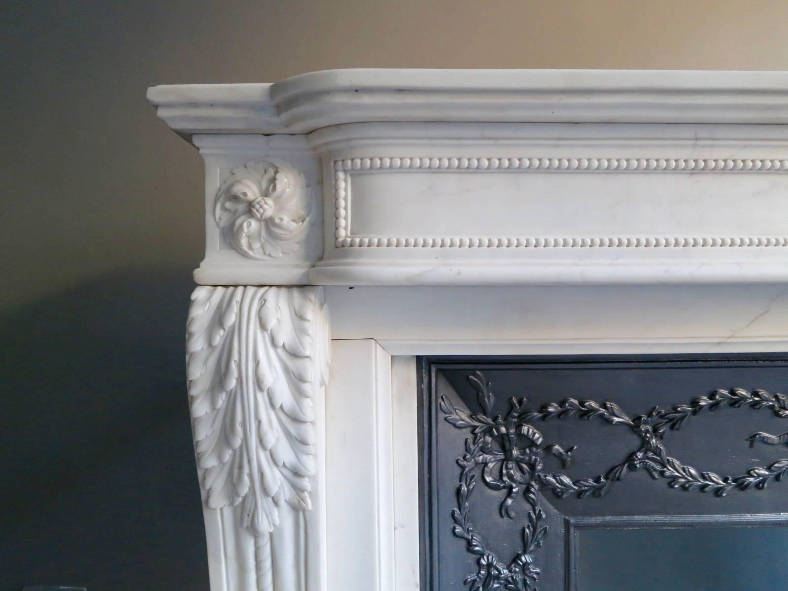 A 20th century Louis XVI style fireplace, in white marble with decorative cast iron interior panel. The jambs with carved acanthus leaf and rope twist design, the bowed frieze with end blocks of carved patarae and carved patarae centre, flanked by