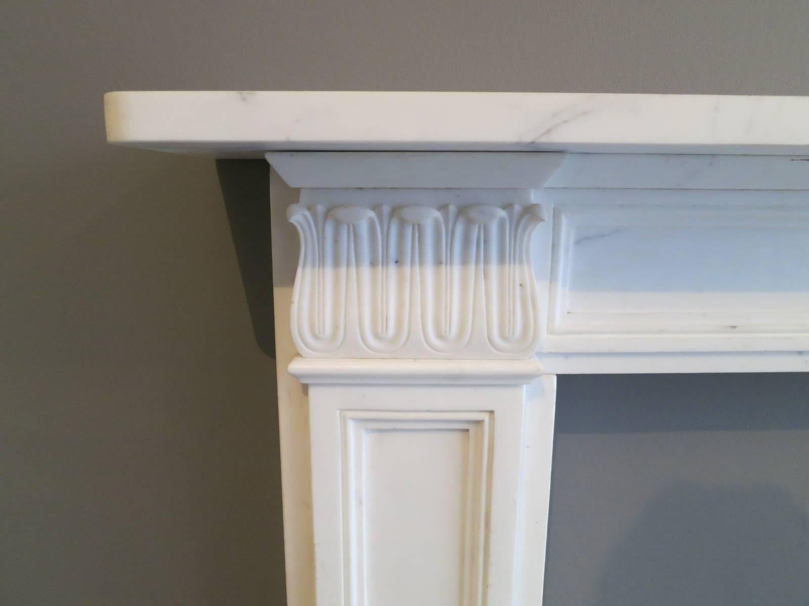 A slightly aged reproduction,  white marble fireplace, with acanthus leaf corner blocks, panelled jambs and conforming frieze. All beneath simple generous mantel. 

Opening Size 91.5cm x 91.5cm 