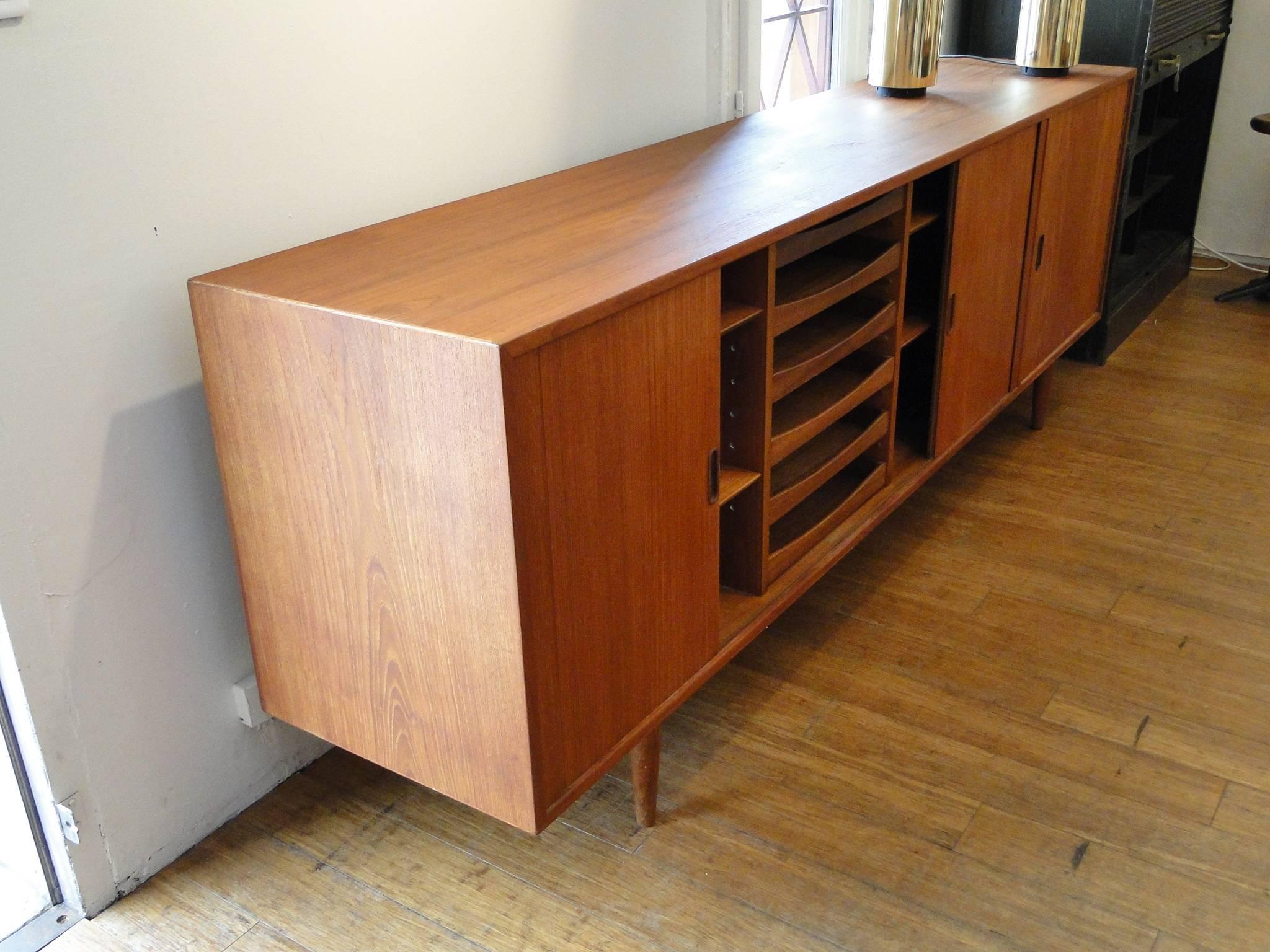 A vintage Danish wooden credenza and sideboard, designed in the Scandinavian Modern style by Arne Vodder for Sibast, with tambour doors, revealing ample shelving space and six pull drawers, with adjacent cabinet with glass shelf. Markings include