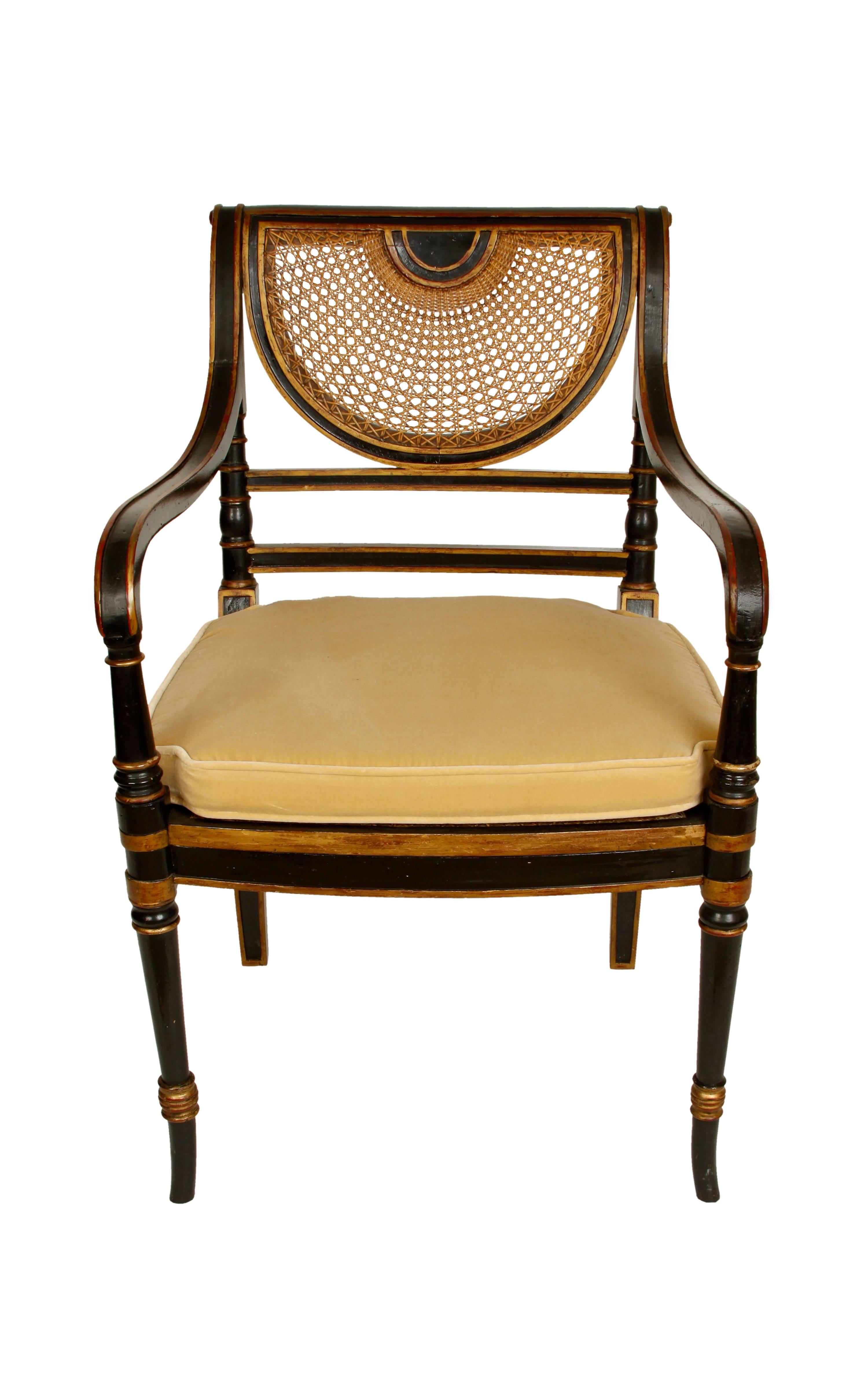 A 1940s Regency style armchair. Black painted wood with gilt detailing and caned seat and crescent back. Removable cushion.