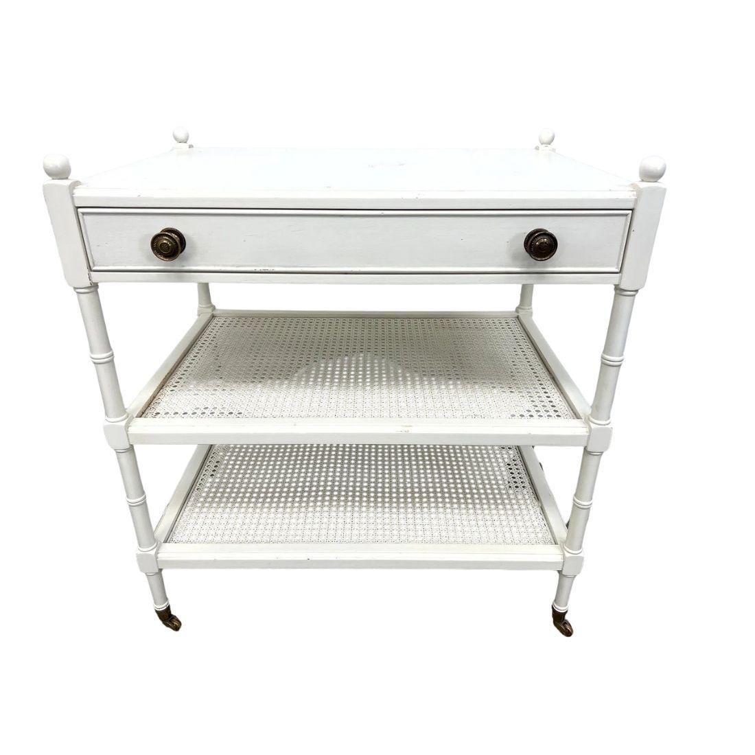 A charming pair of three-tier side tables featuring a faux bamboo frame with a crisp white painted finish, evoking classic British Colonial and Hollywood Regency styles. Each table is thoughtfully designed with a single drawer for storage and two