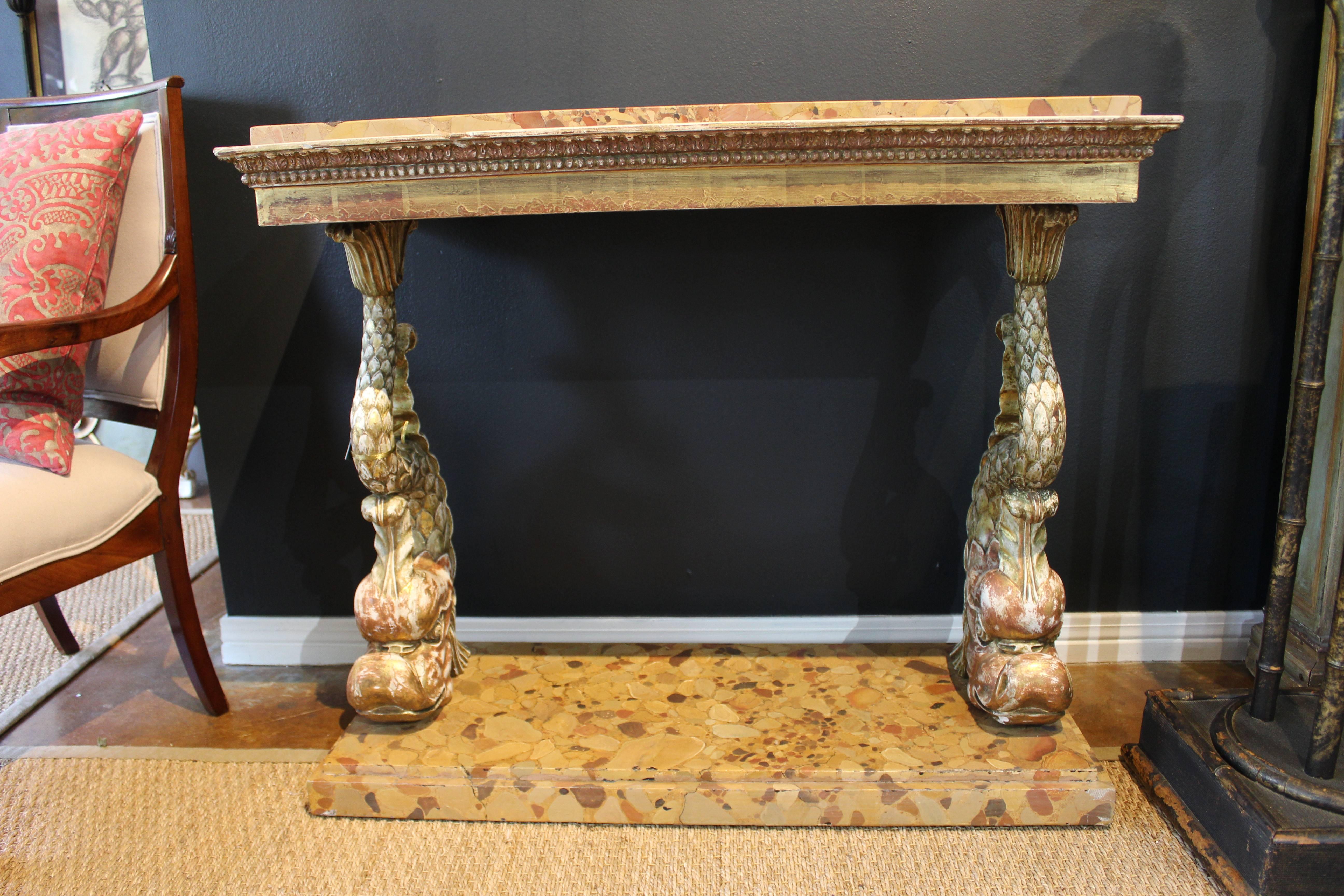 Pair of gorgeous consoles with giltwood structure and solid peach and ochre hued stone tops and bases. Carved Regency Italianate dolphins support each console. Designed to be used against a wall, not freestanding.