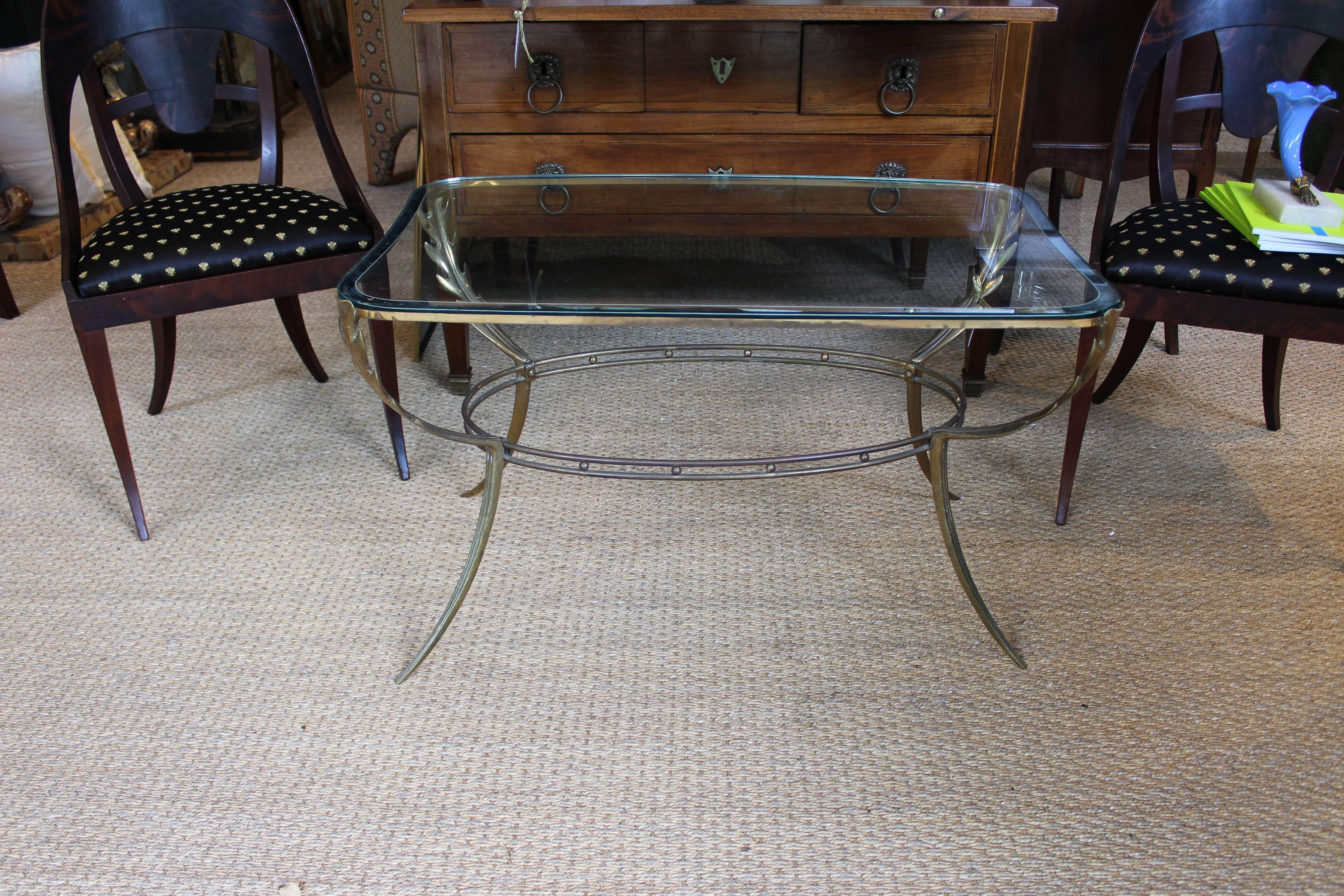 Italian brass coffee table with leaf detail legs on fluted supports. Top is glass with curved frame.
