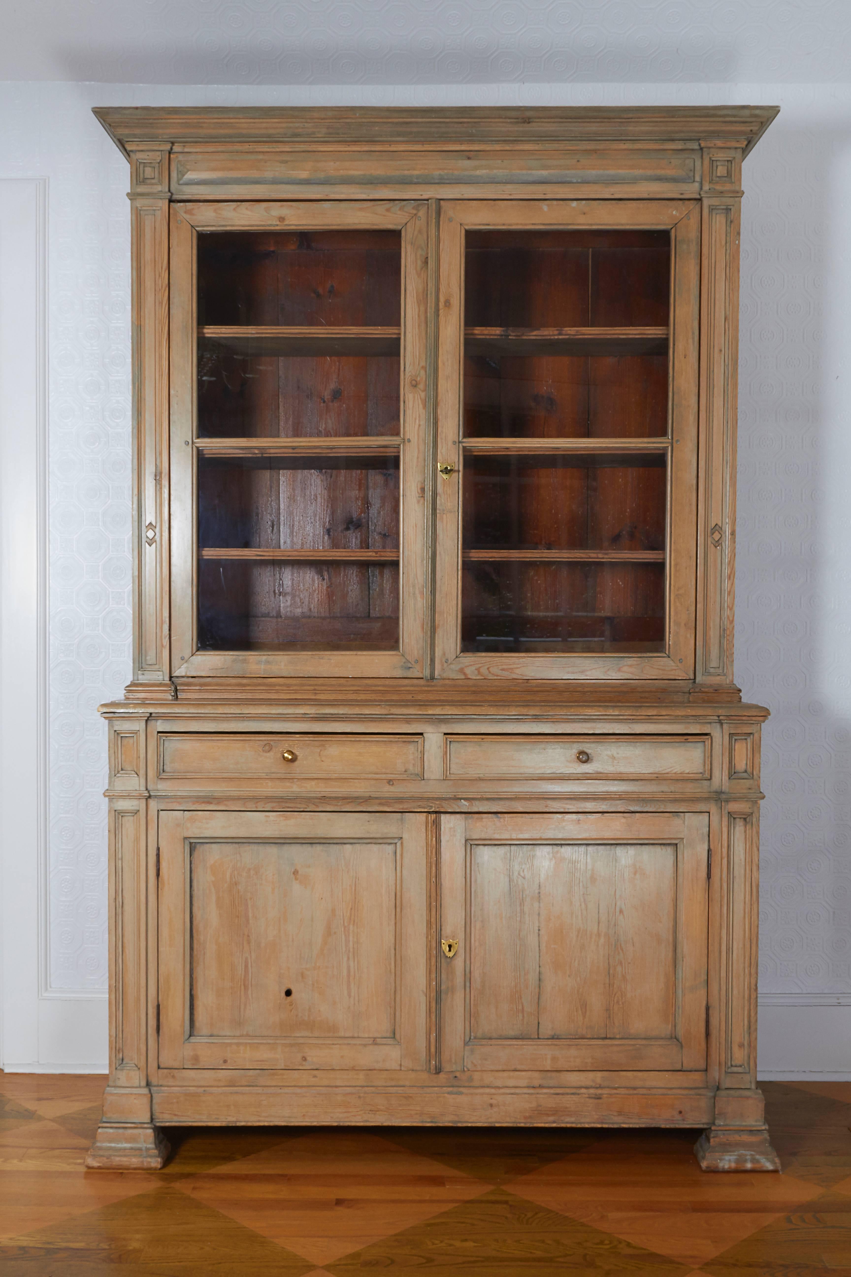 With very attractive patination and faded color; the upper section with glass-front doors opening to shelves; the lower part fitted with two drawers and two doors opening to shelves; on block-form feet.