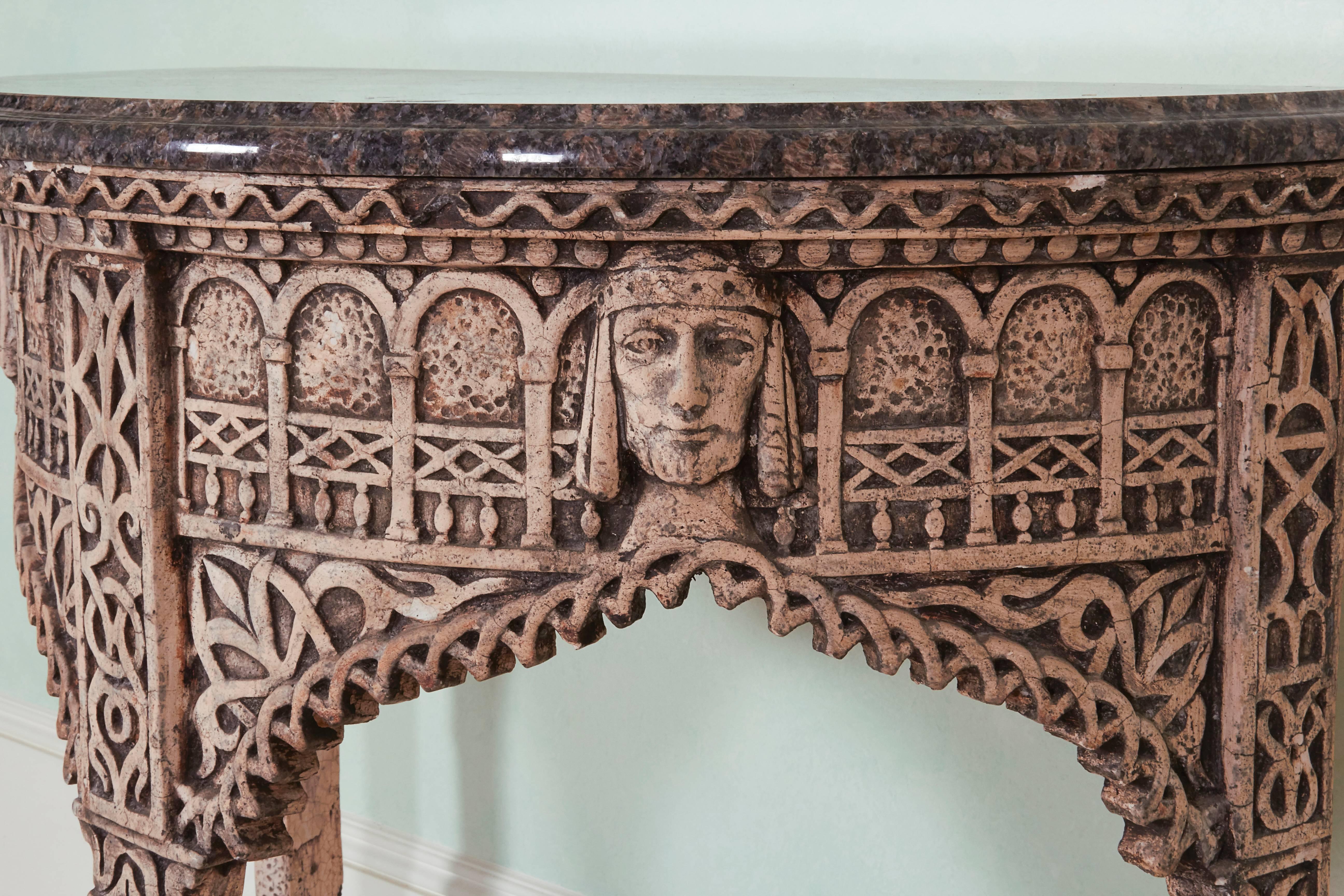 With sapphire blue granite top; the table base with gesso decoration carved in low relief with romanesque scrollwork, medieval masks and an arcaded frieze above an ogee-arched edge.