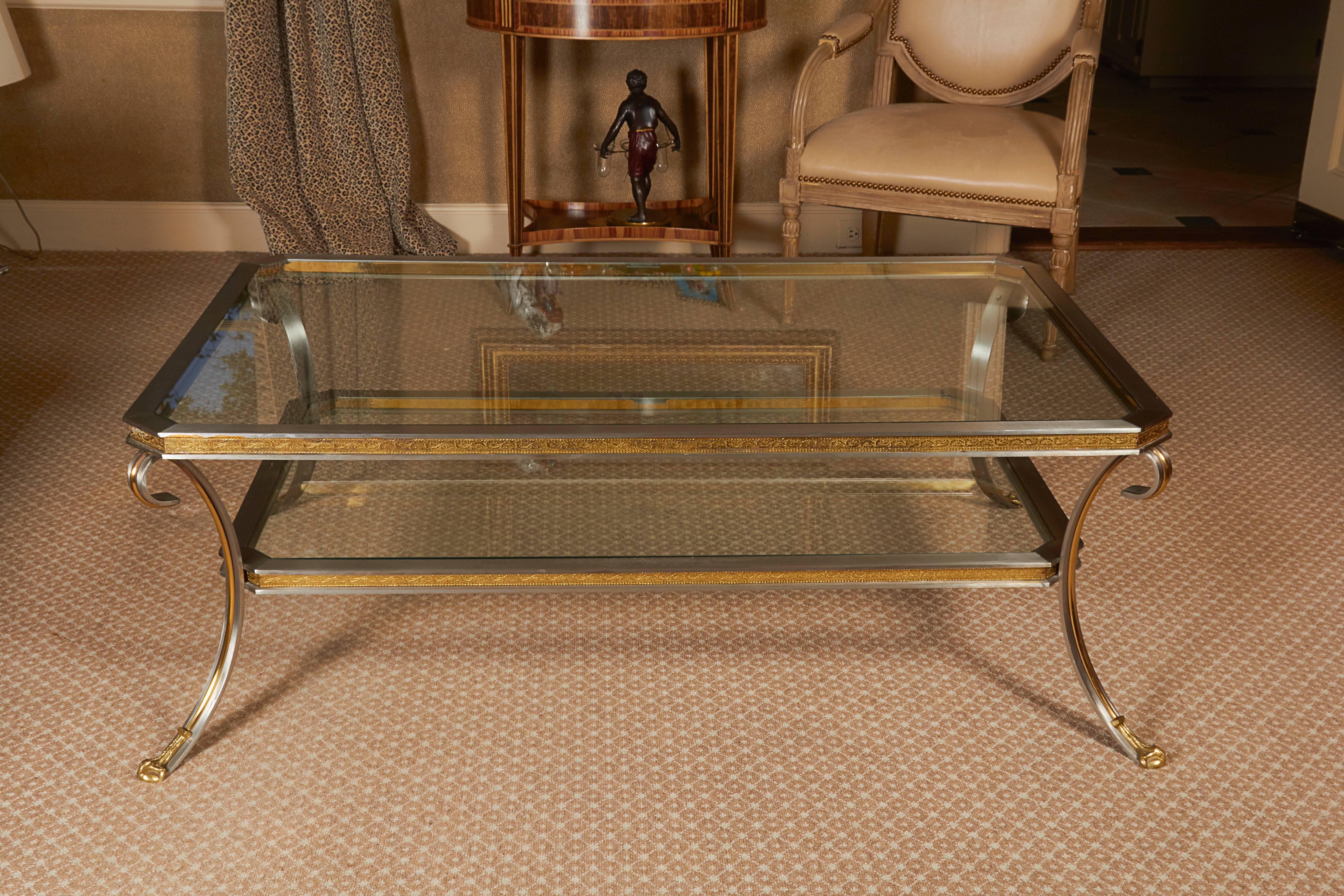 The rectangular glass top with canted corners set within the metal frame over a conforming glass shelf; raised on brass channeled volutes terminating in brass feet.