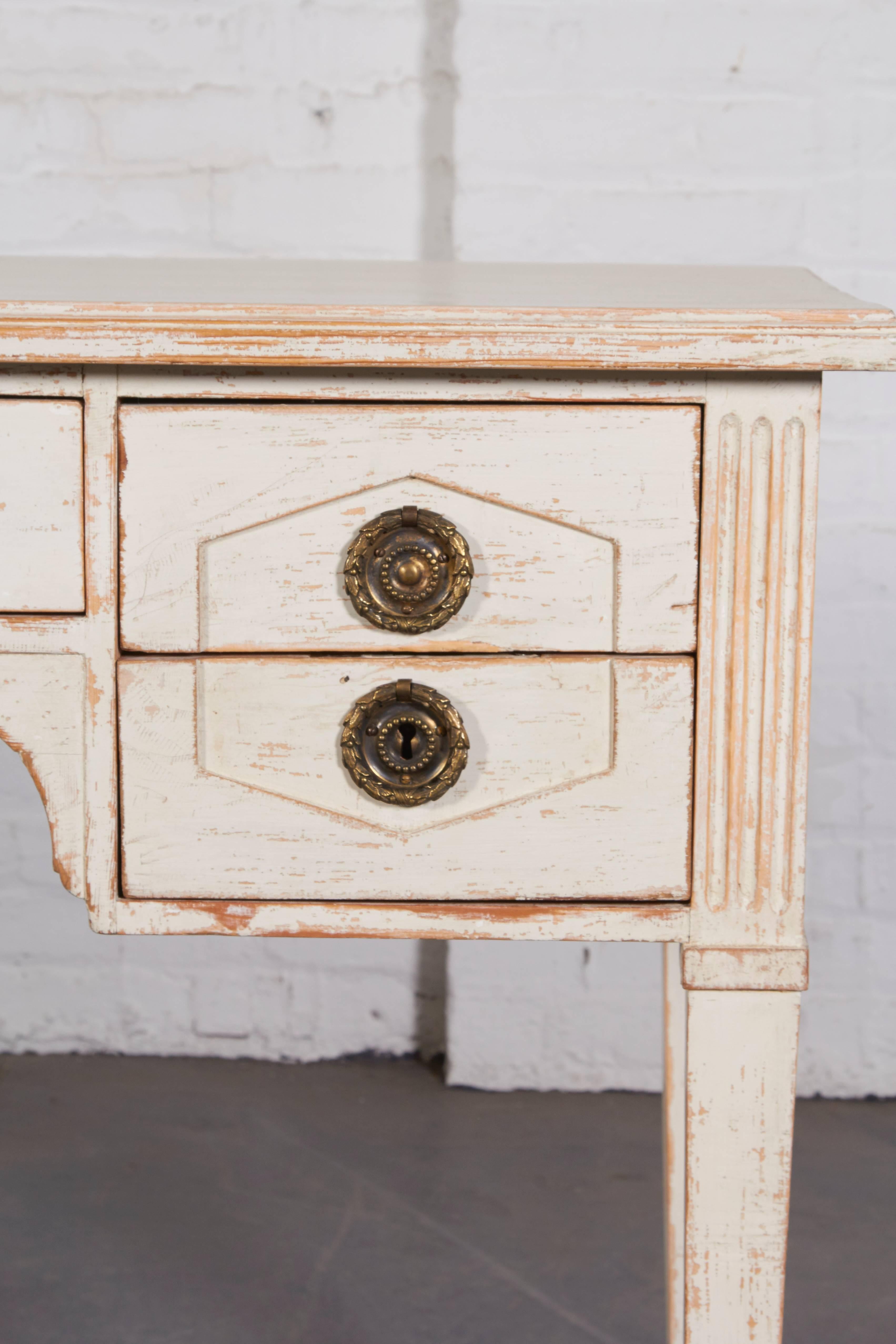 The rectangular top over a central frieze drawer and shaped apron flanked by two short panelled drawers; raised on square tapering legs with attractive distressed white finish; drawers lined with marbled paper.