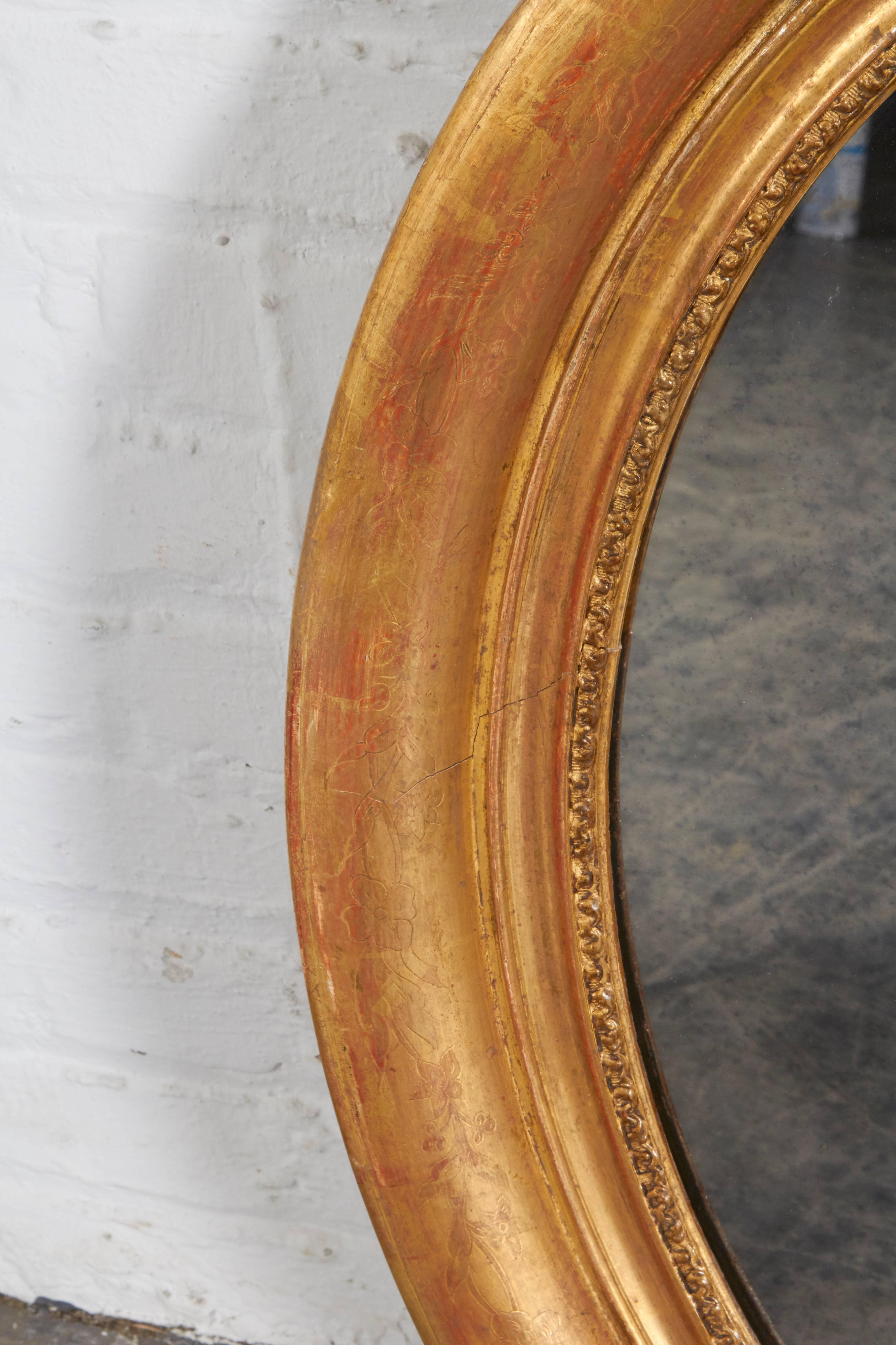 The antiqued mirror plat set within a conforming giltwood frame with delicately incised floral sprays and birds.