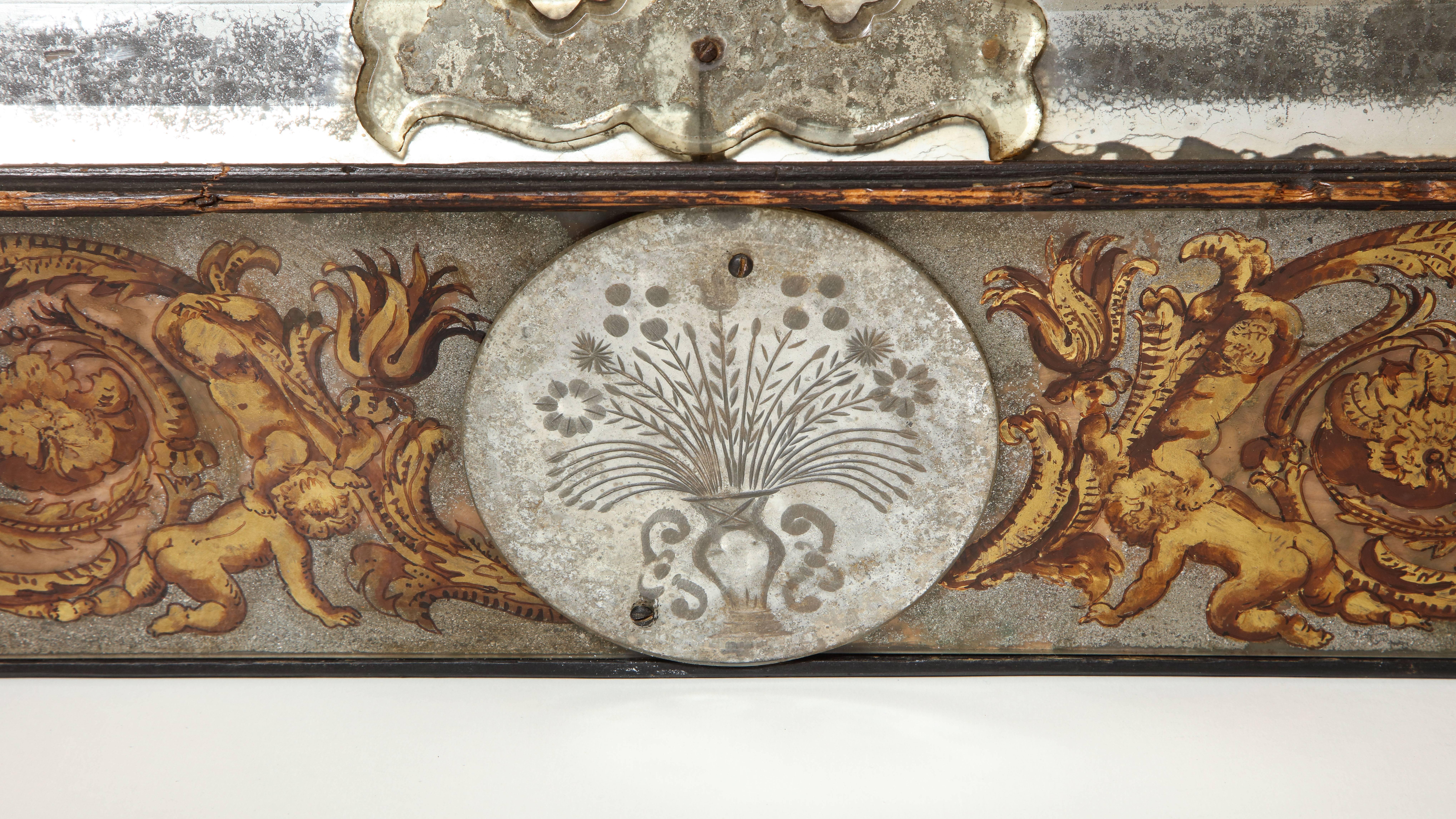 The rectangular plate in a faceted bevelled surround within the conforming verre églomisé frame decorated with scrolling foliage, putti and dragons in gold and red and applied with roundels of spread eagles and vases of flowers, inscribed to reverse