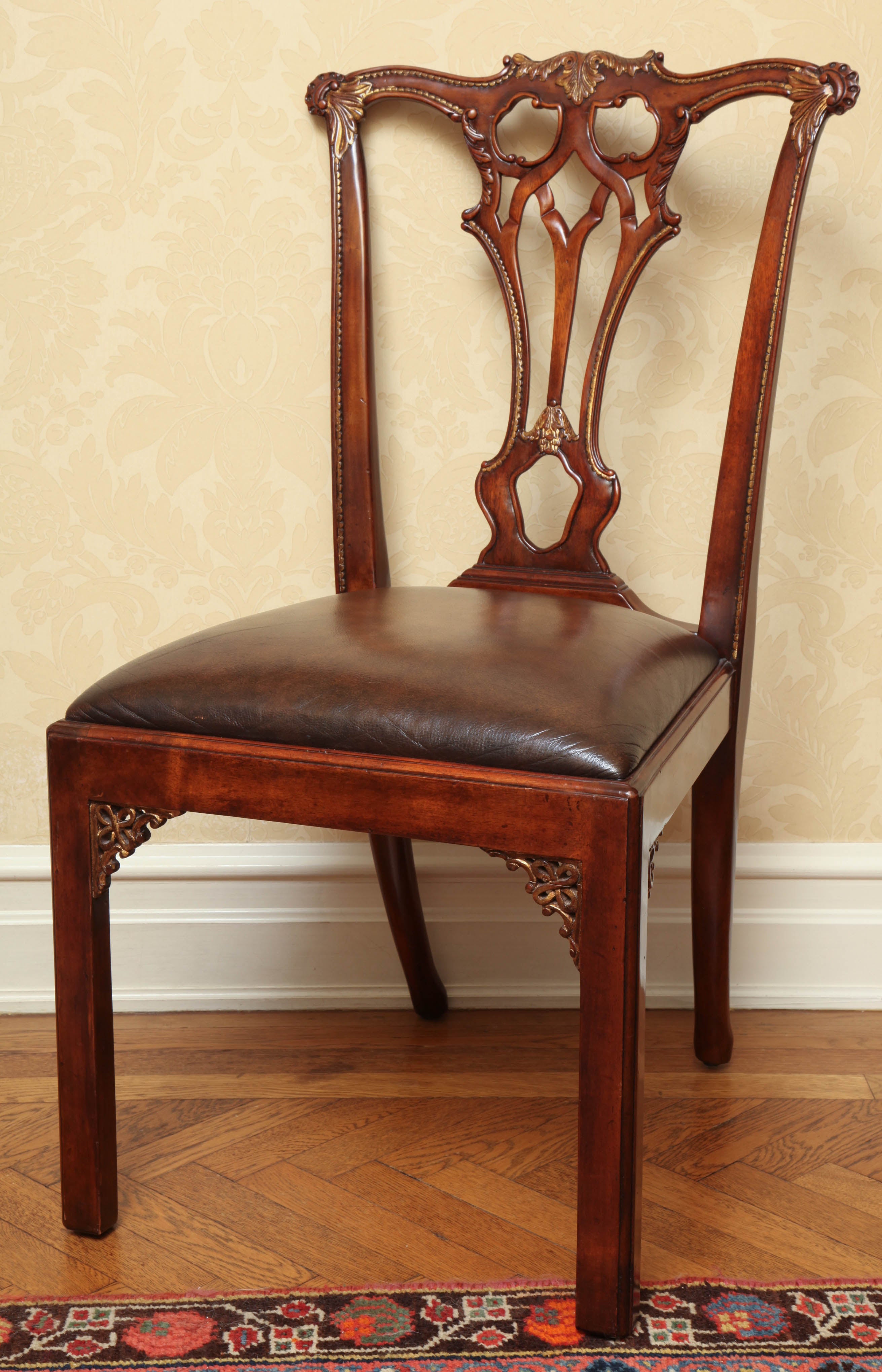 Each mahogany side chair after a period Chippendale design with parcel-gilt decoration and drop-in leather seat.
