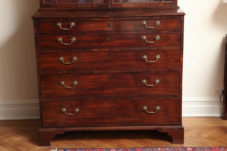 The secretaire bookcase features richly hued and finely figure veneers. The upper part surmounted by a swan's neck cornice, over the dentil-molded frieze and two astragal-glazed doors opening to three adjustable shelves; the lower part comprised of