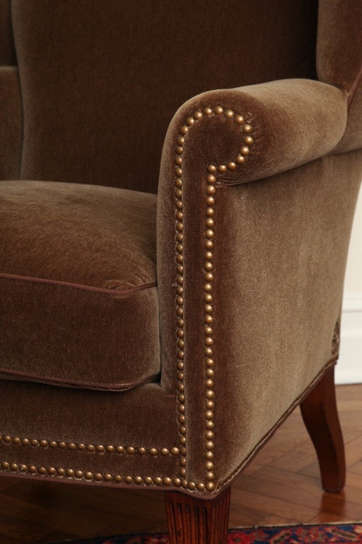 Each wingback armchair upholstered in mohair with an arched back and wings set above a cushion seat enclosed by overscrolled arms. On fluted tapering legs terminating in brass sabots. Made by Theodore Alexander.