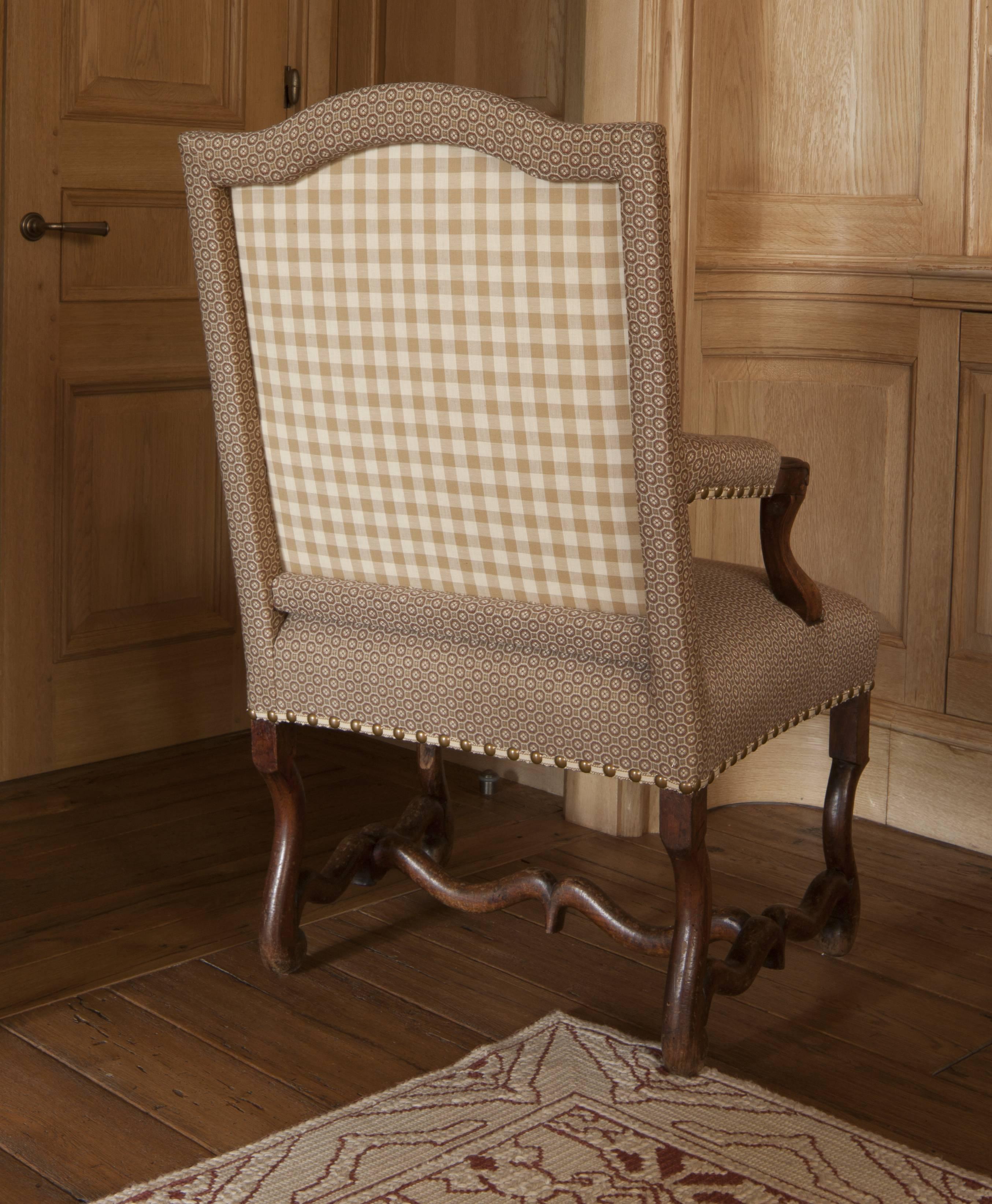 Armchair with arched upholstered back issuing downswept padded armrests; the over upholstered seat raised on Os de Mouton legs joined by stretchers. 

  
