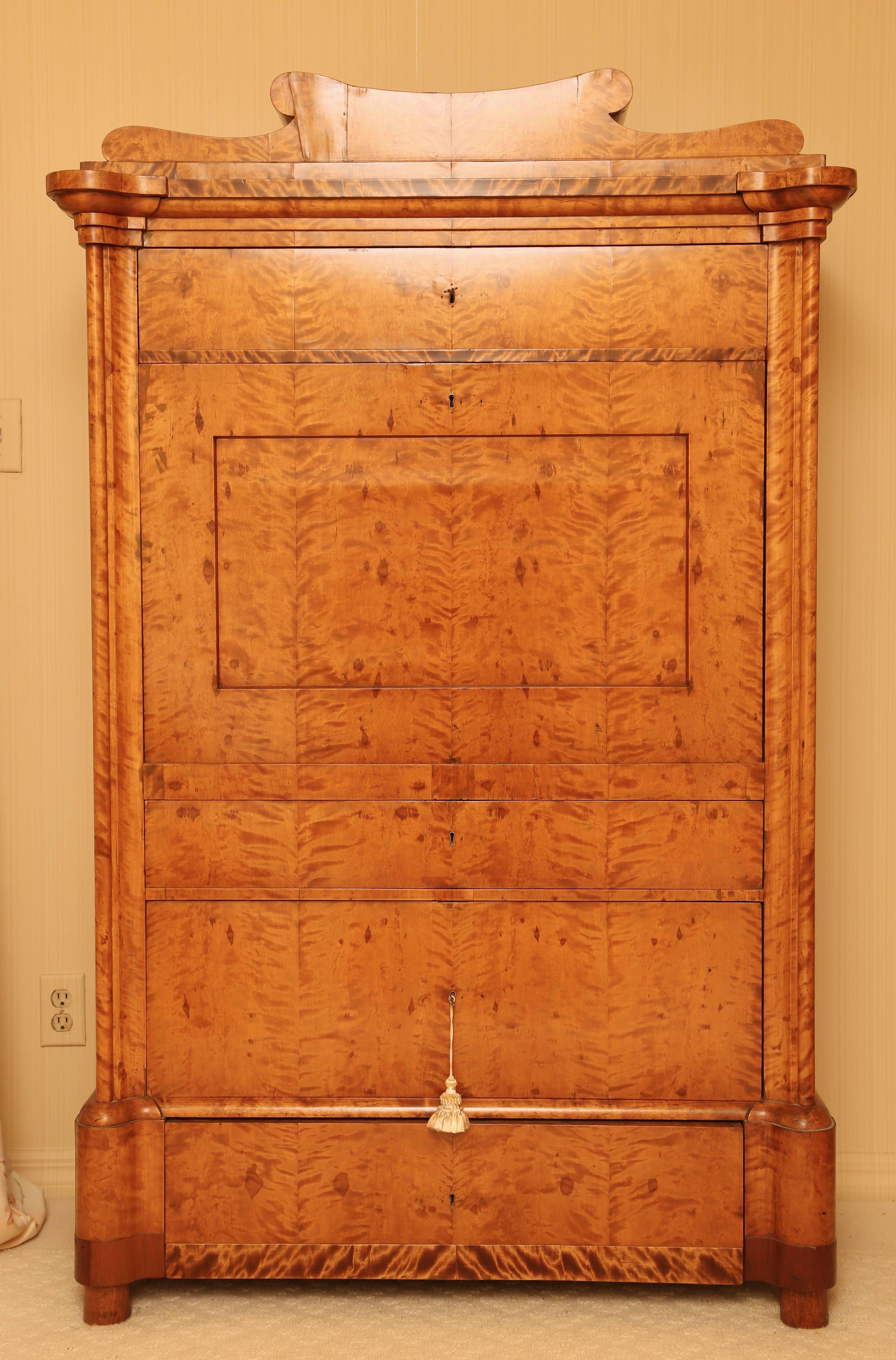 With beautifully figured bookmatched veneers; the shaped cornice over a frieze drawer and fall front inclosing an arrangement of drawers around a prospect door, all with walnut banding and foliate inlay, over three drawers; on cylindrical feet.