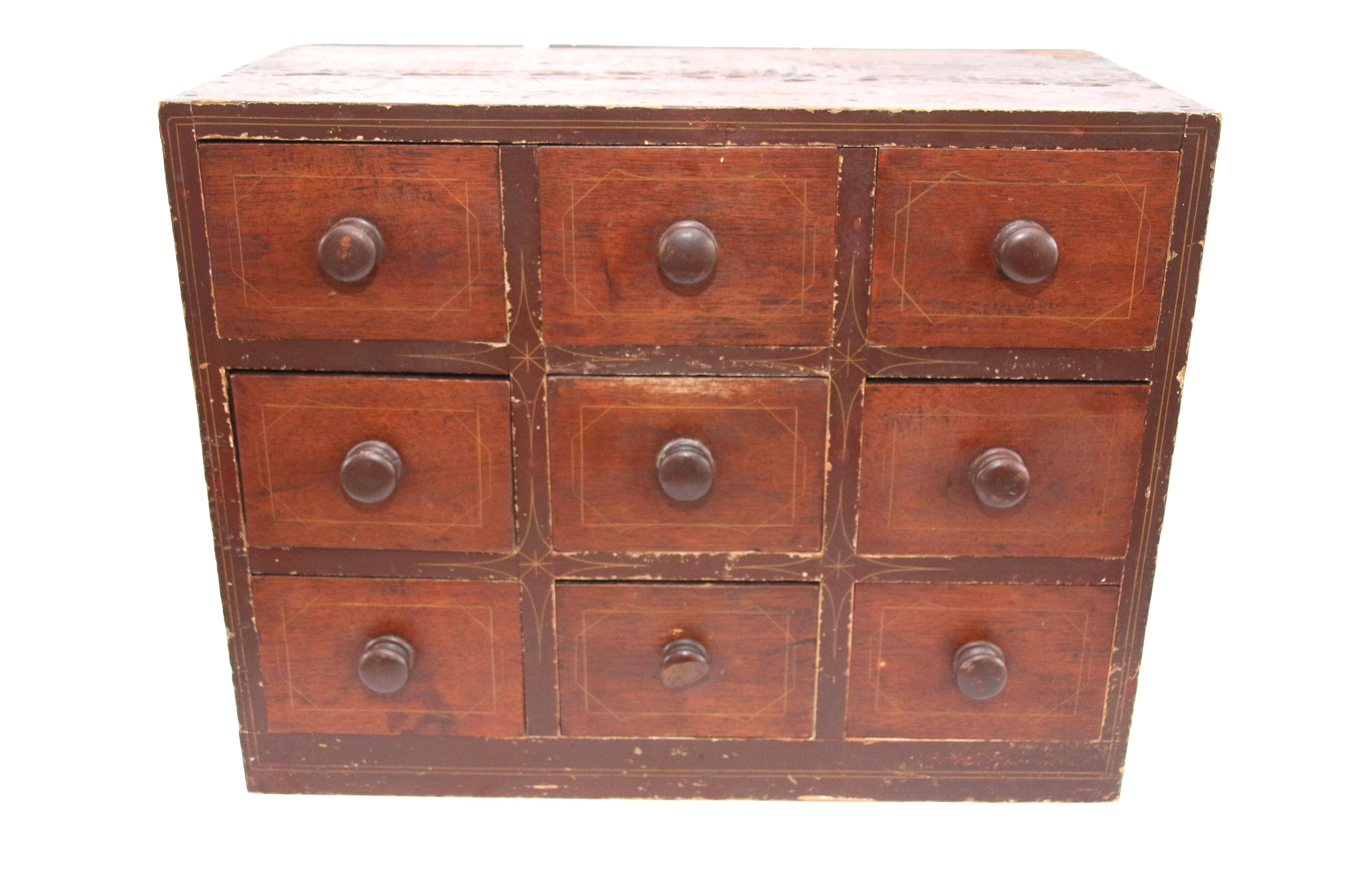19th century paint decorated apothecary or spice chest made from butternut and basswood. The counter top nine-drawer example in original red paint with yellow pinstripe. The drawer fronts stained dark red with yellow pinstripe, each drawer fitted