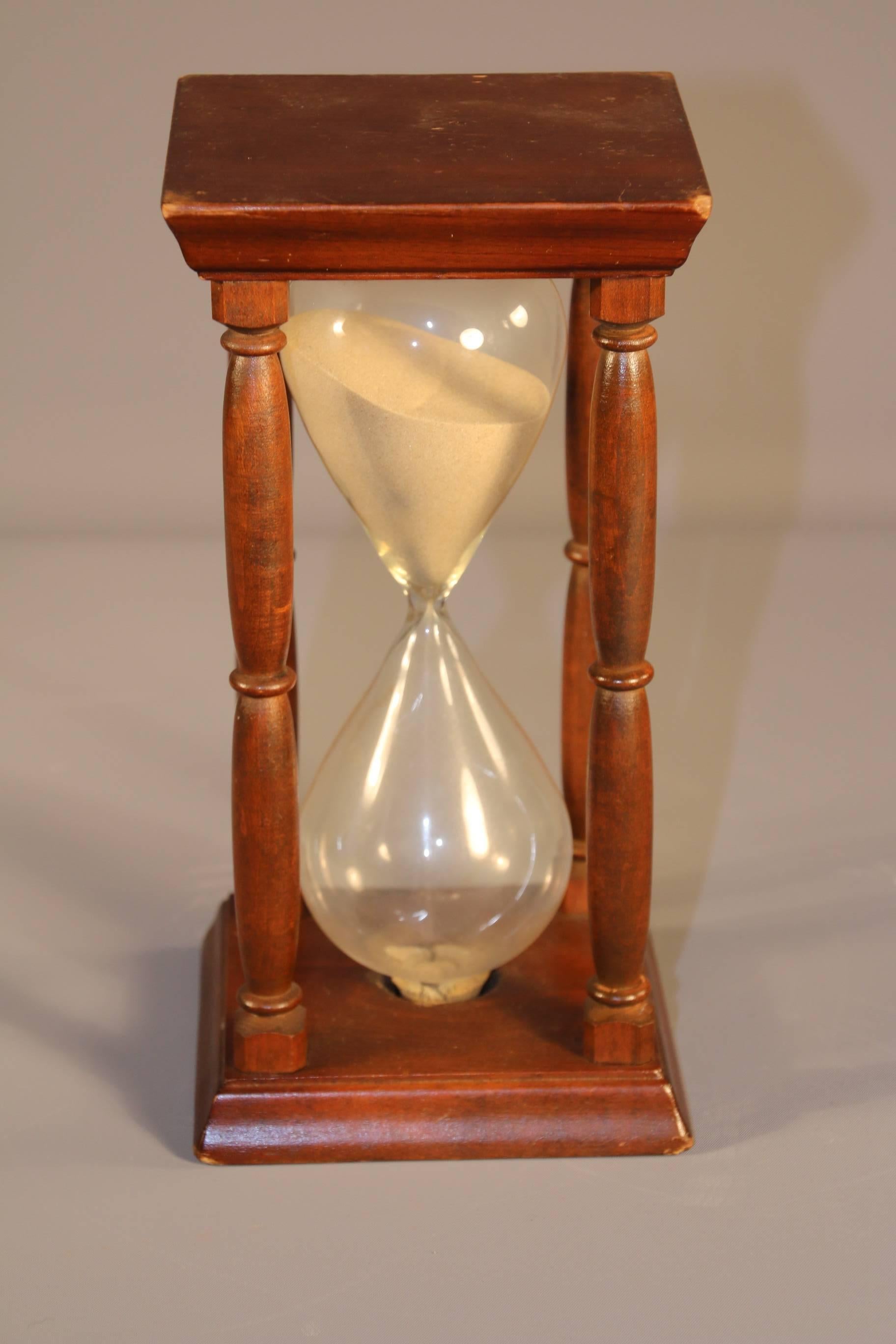 Mid-19th century sand-filled hourglass contained within a wooden stand with square top and base and four turned spindles. Time: 1 hour.

Measures: 9” H X 4 ½” W.