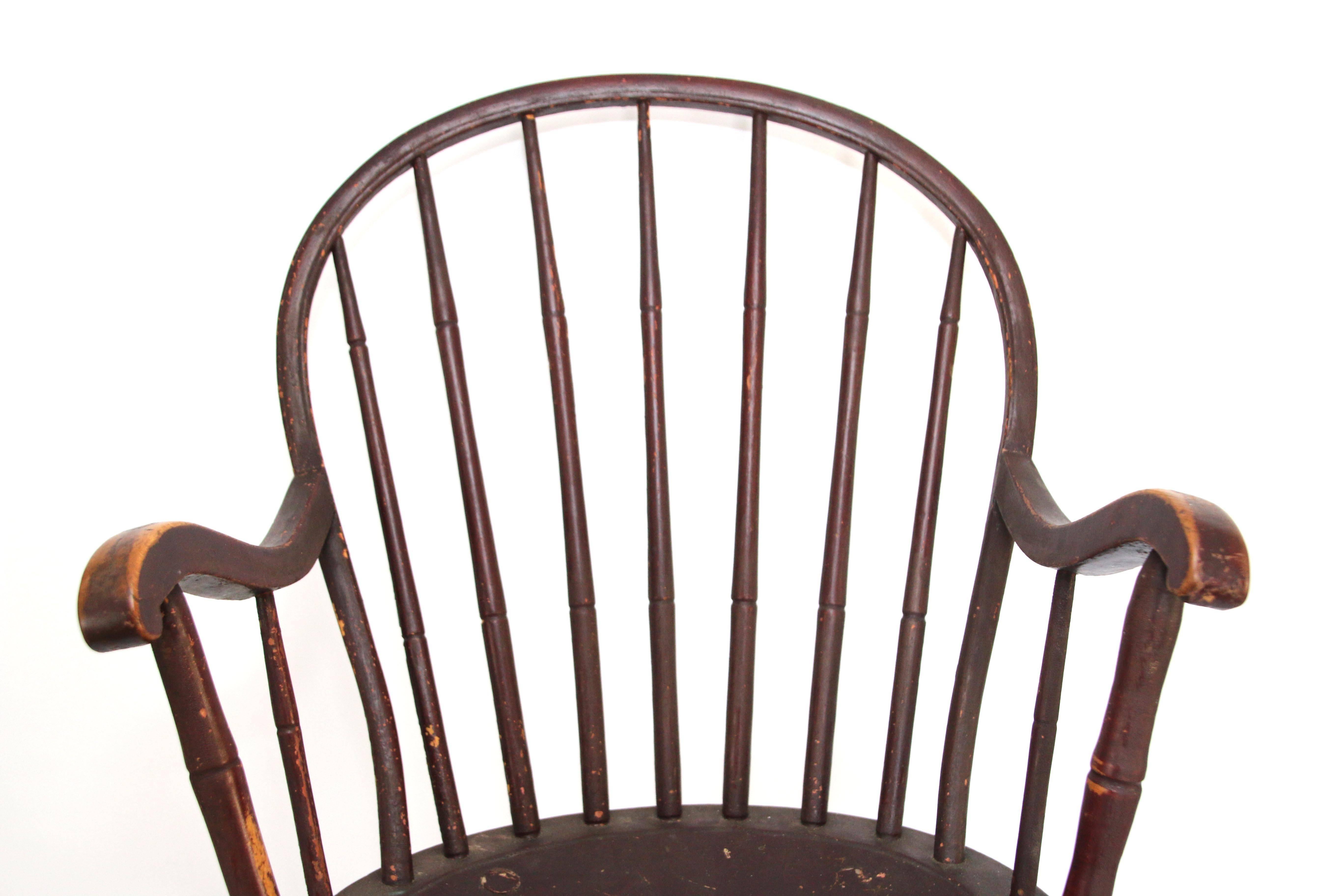 Bowback windsor armchair in red paint. The bowed crest rail above nine spindles, continuing to serpentine arms to the hoop back and all joined to the shield-shaped seat, raised on simulated and swelled splayed legs joined by a similar H-stretcher in