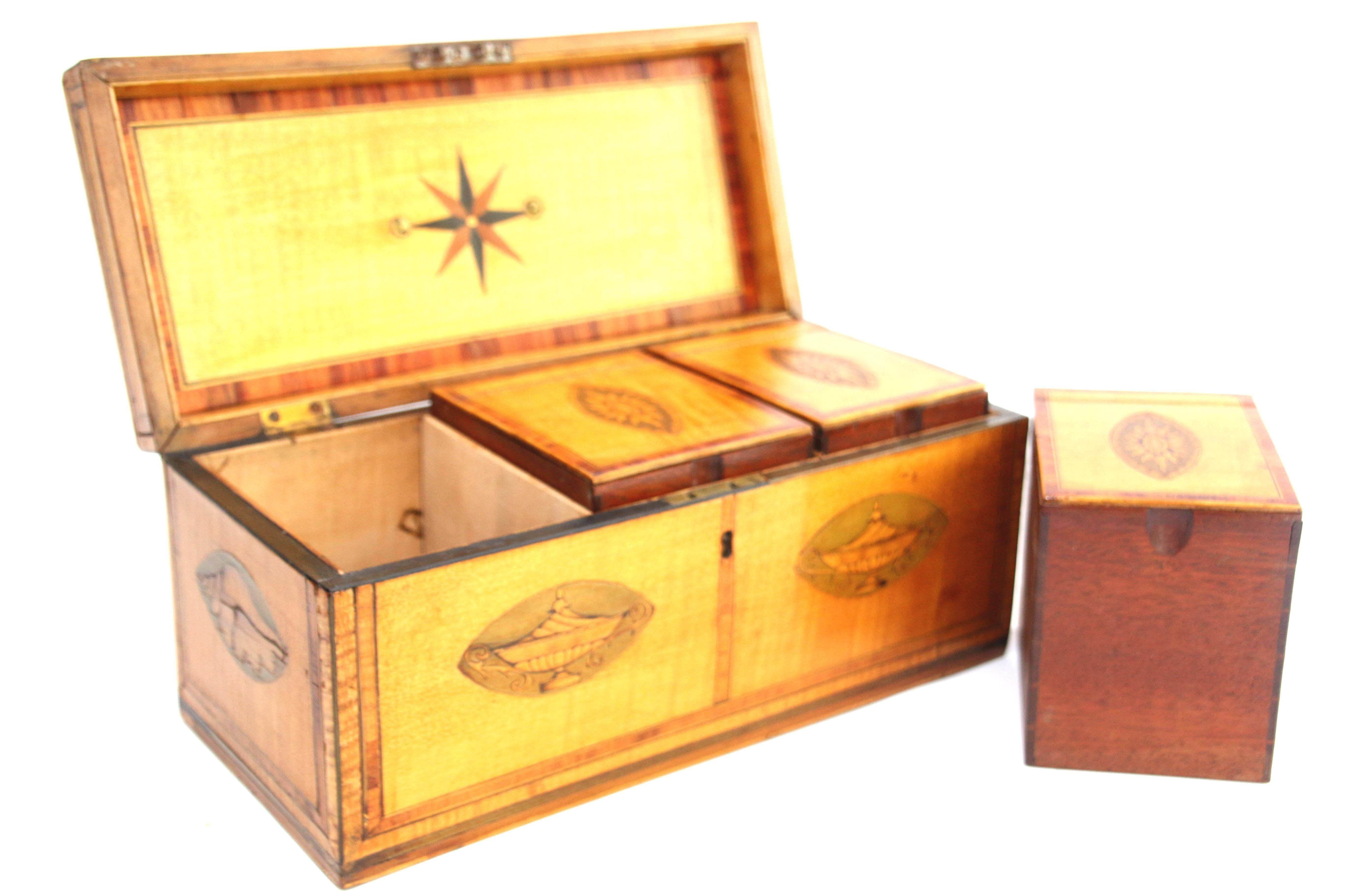 George III rectangular satinwood tea caddy with crossbanded borders, two inlaid leaf motifs flanking the brass handle to the lid along with two inlaid urns decorating the front, and conch shell inlay on both sides. Interior lid retains compass star