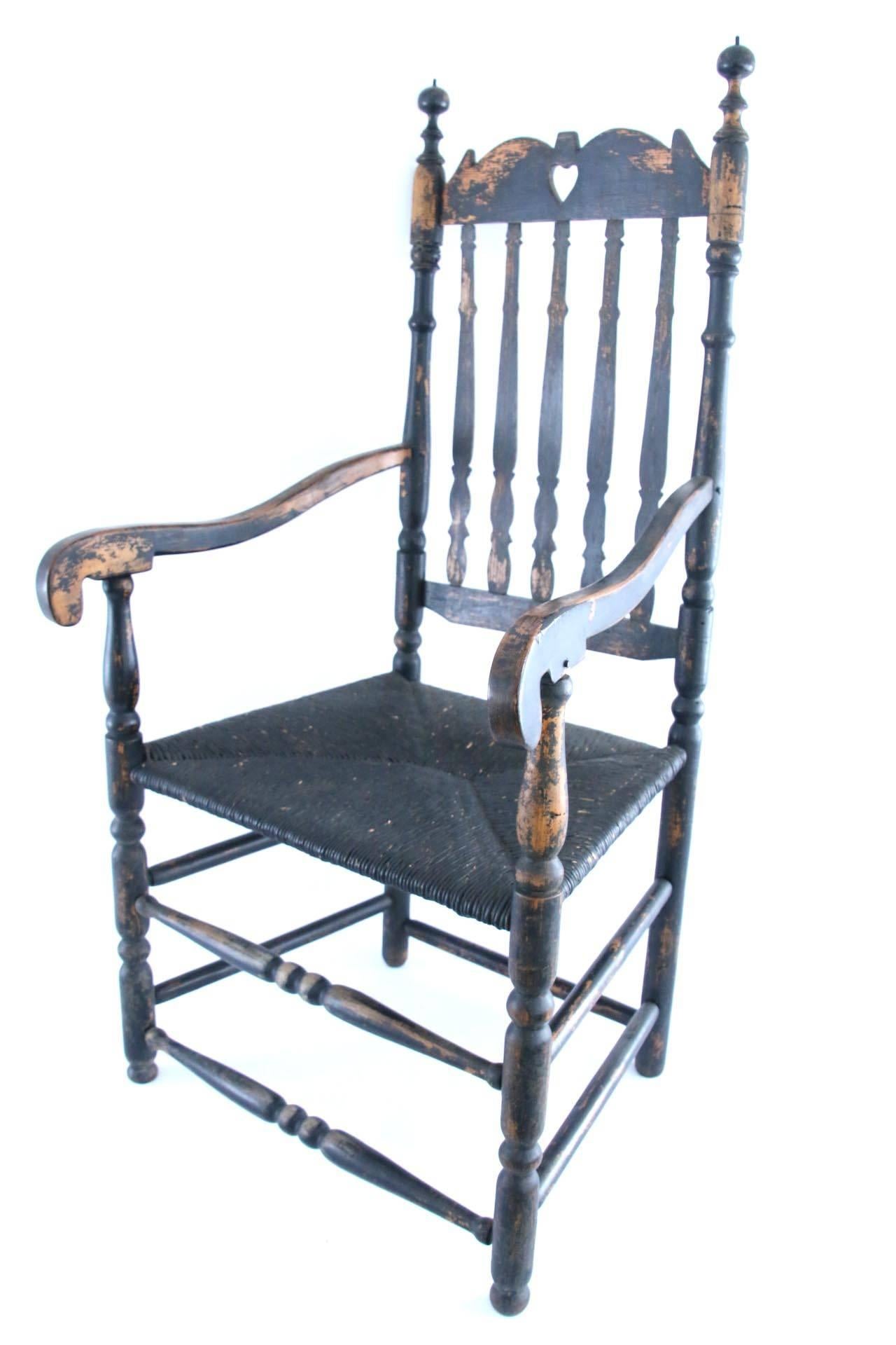 18th century black painted banister-back armchair with shaped cresting and heart cut-out along with vase-and ring-turned stiles possessing bulbous finials and scrolled handholds, all supported on vase-and ring-turned legs and joined by double