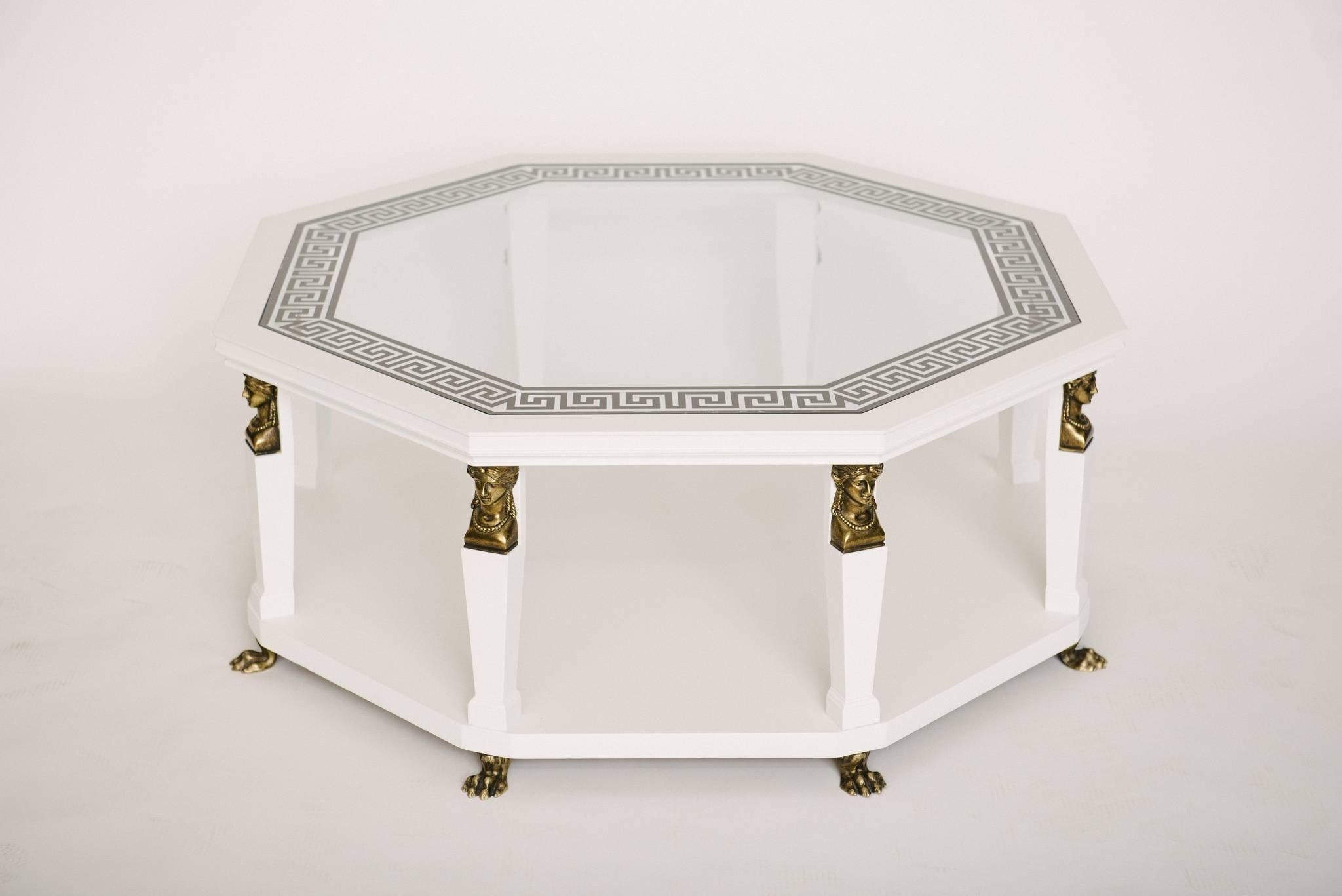 A timeless vintage baker white painted wood and glass cocktail table with Greek key detailing, brass caryatids and lions feet.