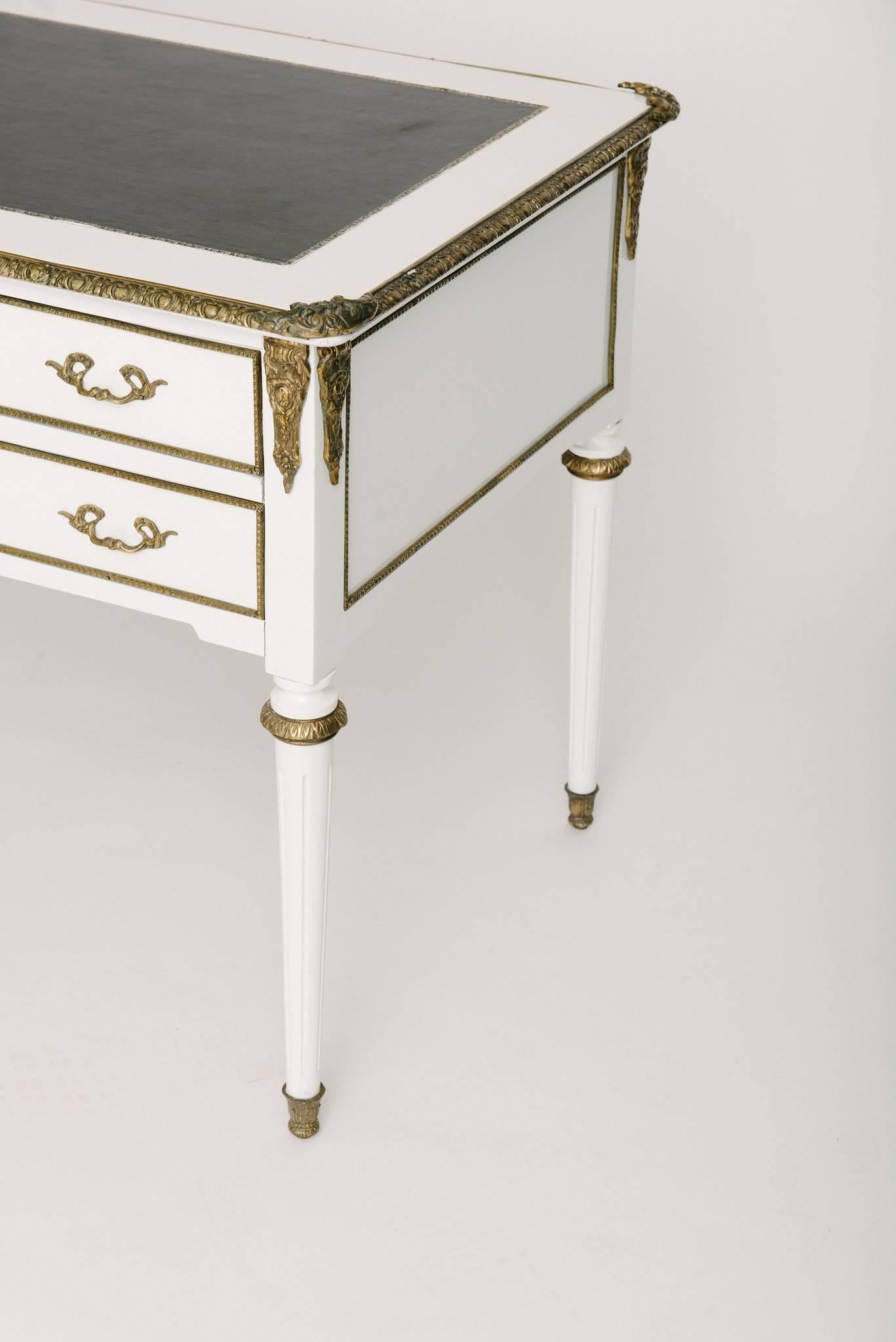 A vintage Louis XVI style white lacquered desk with ormolu detail and black leather top.