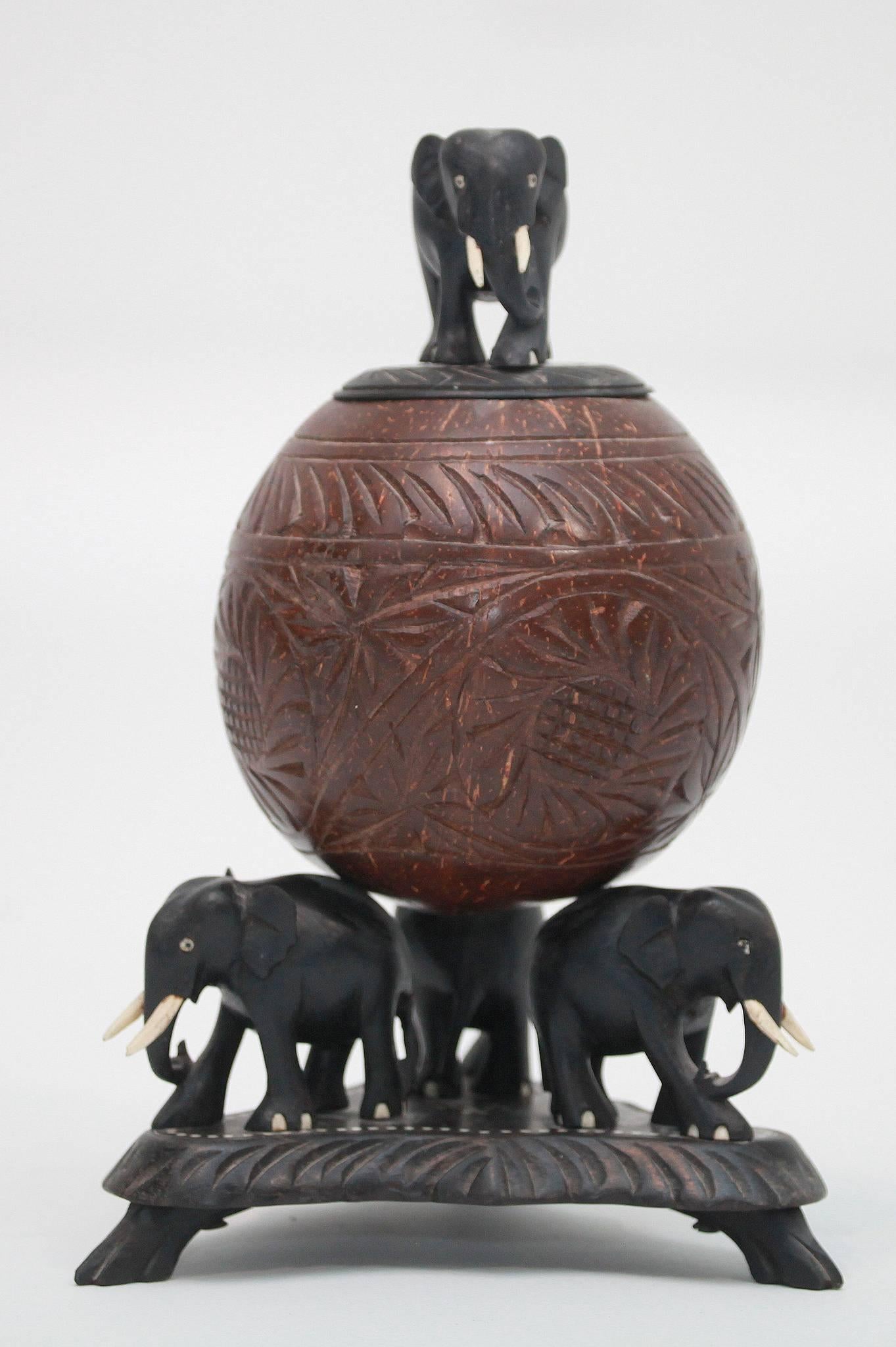 Hand-carved ebony elephants on footed base holding up a carved spherical coconut box and lid.